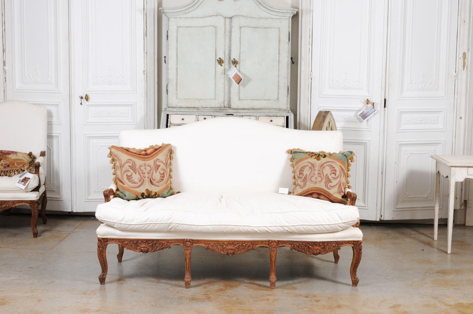 A French Régence style carved wood canapé from the mid-19th century, with new upholstery. Created in France in the early years of Emperor Napoleon III's reign, this Régence style three-seat sofa features a slightly slanted camelback, flanked with