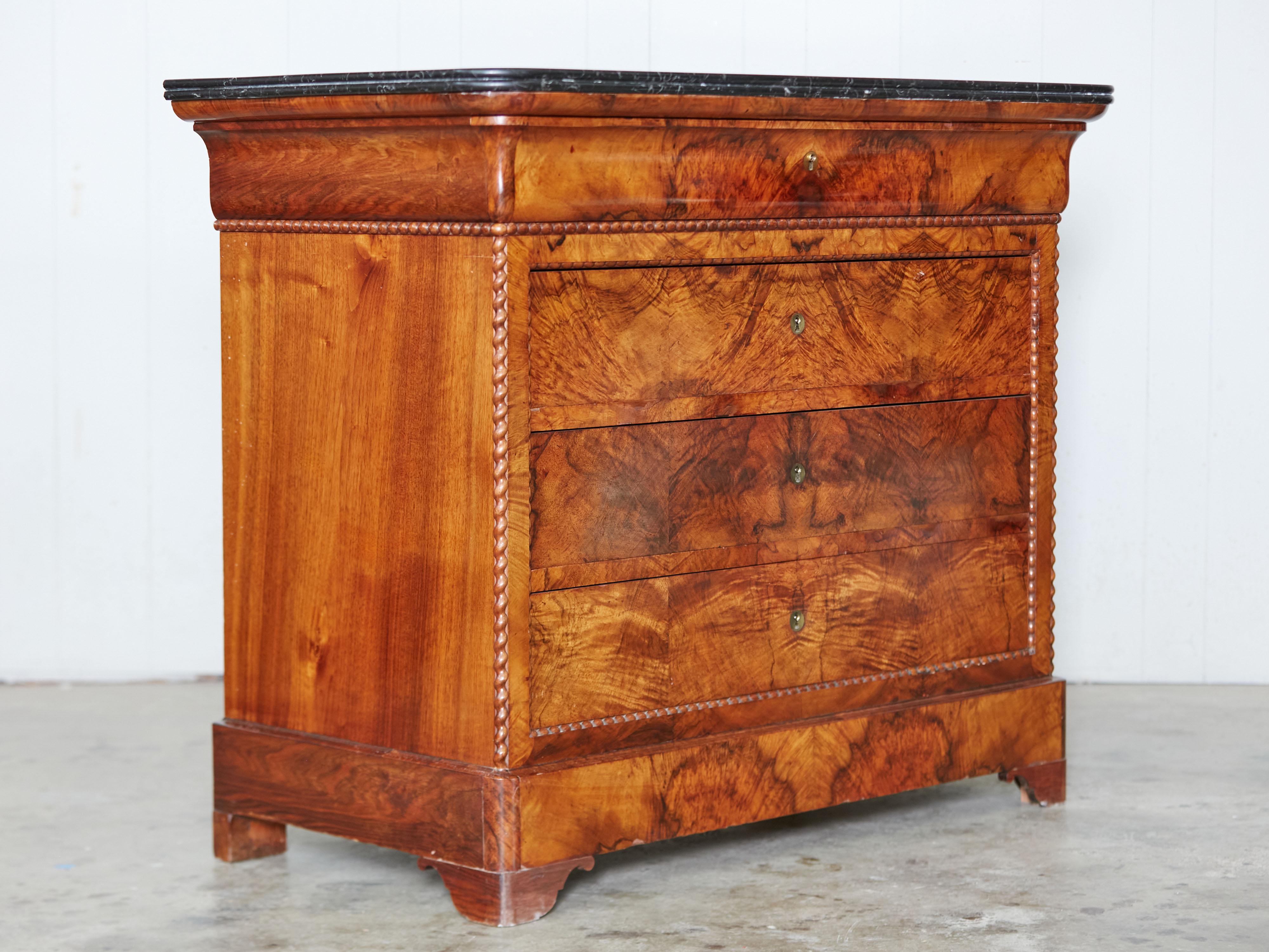 A French Louis-Philippe style walnut commode from the late 19th century, with black marble top and four drawers. Created in France during the third quarter of the 19th century, this walnut commode features a black rectangular top with rounded