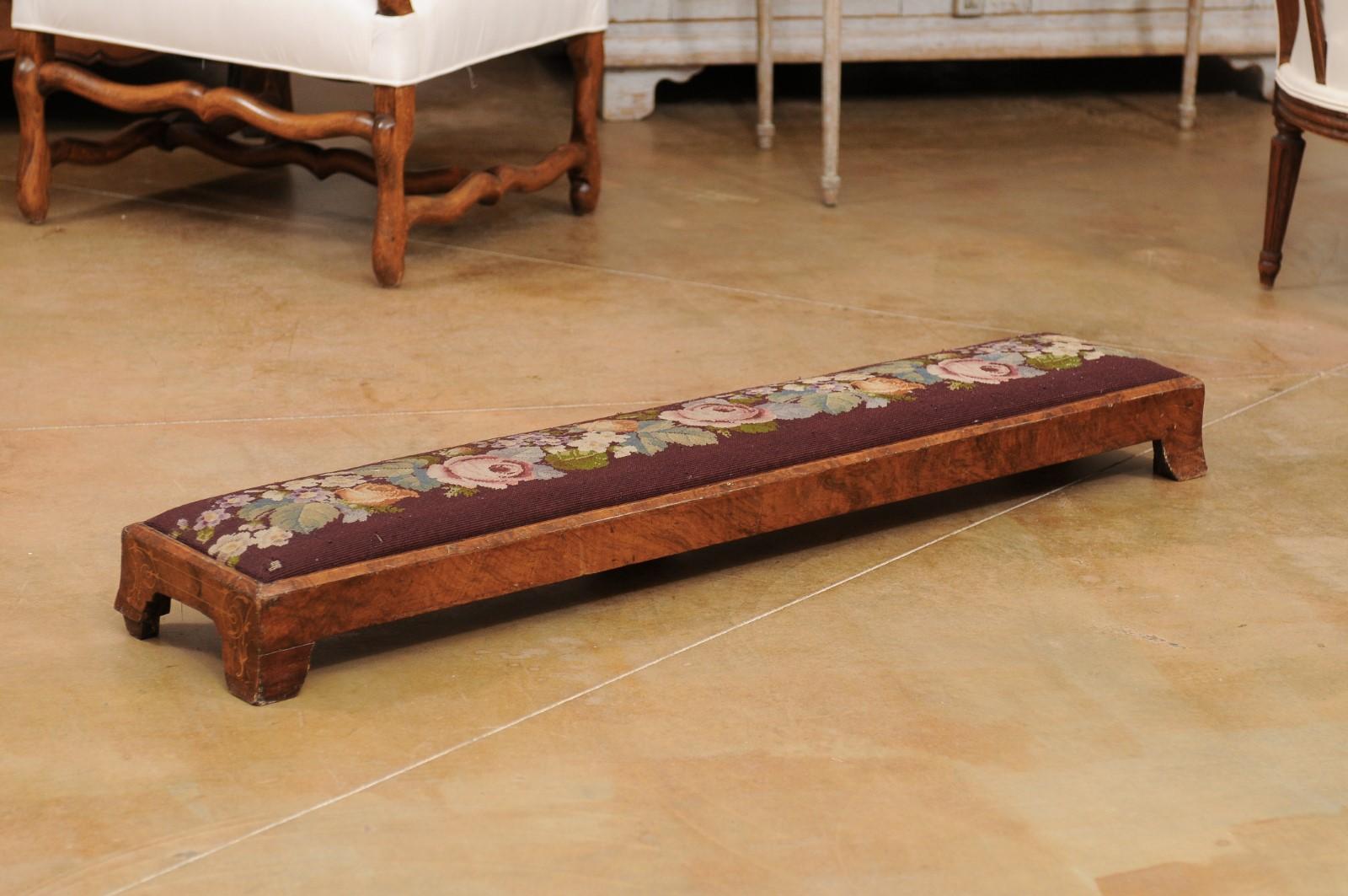 A French Napoléon III period long needlepoint footstool from the mid 19th century, with floral décor and splayed bracket feet. Created in France during the reign of Emperor Napoléon III, this footstool features a long narrow top covered with a