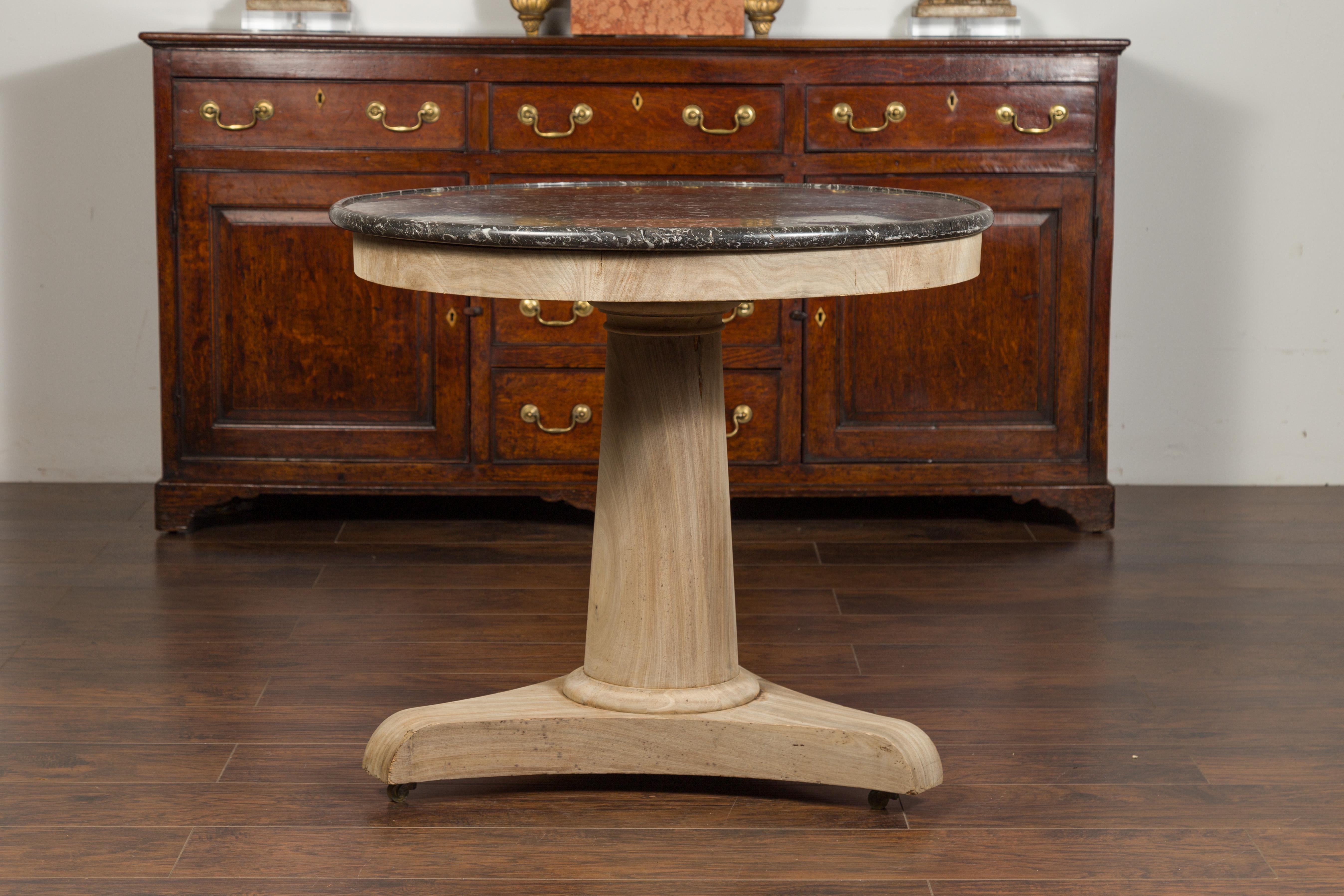 A French Empire style freshly bleached walnut side table from the 1870s, with dark grey variegated marble top and casters. Created in France at the end of Napoleon III's reign, this round pedestal side table presents the stylistic characteristics of