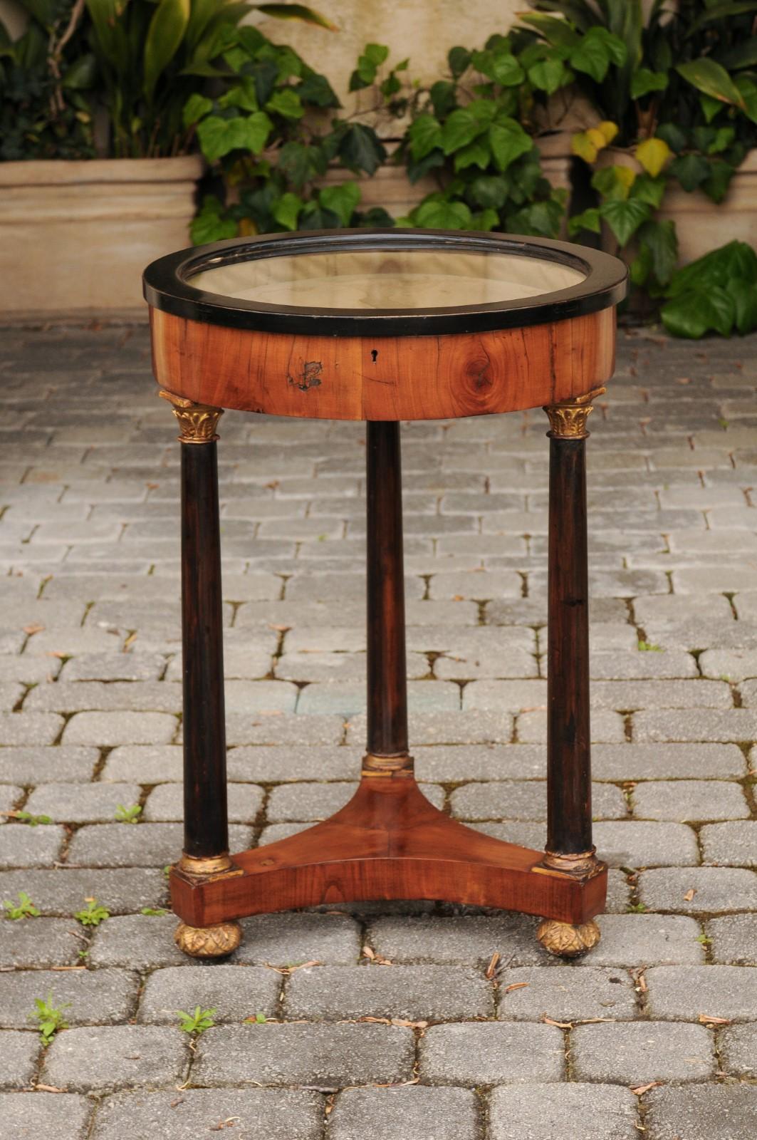 A French Empire style walnut gueridon table from the late 19th century, with vitrine top, corinthian columns, ebonized and gilt accents. Born in France during the third quarter of the 19th century, this exquisite French gueridon table features a