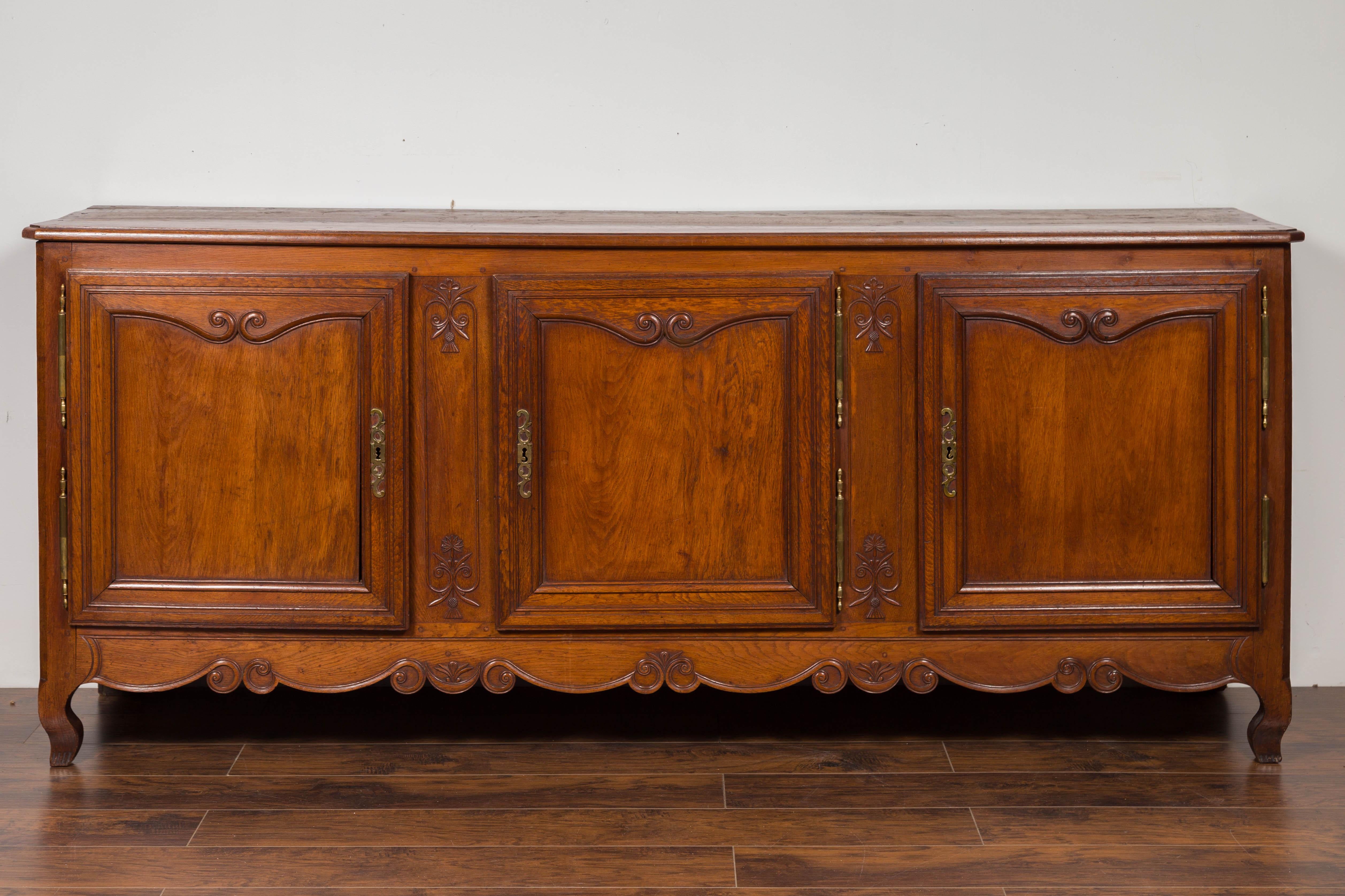 A French three-door oak enfilade from the late 19th century, with scrolled motifs and cabriole legs. Born in France at the end of Emperor Napoleon III's reign, this oak enfilade features a rectangular top with canted corners in the front, sitting