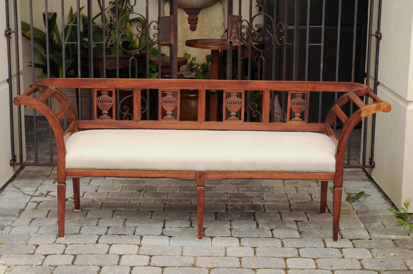 A French fruitwood settee from the late 19th century, with carved urns, out-scrolling arms and new upholstery. Born in France at the end of Emperor Napoleon III's reign, this settee features an exquisite pierced back, adorned with carved urns. Two