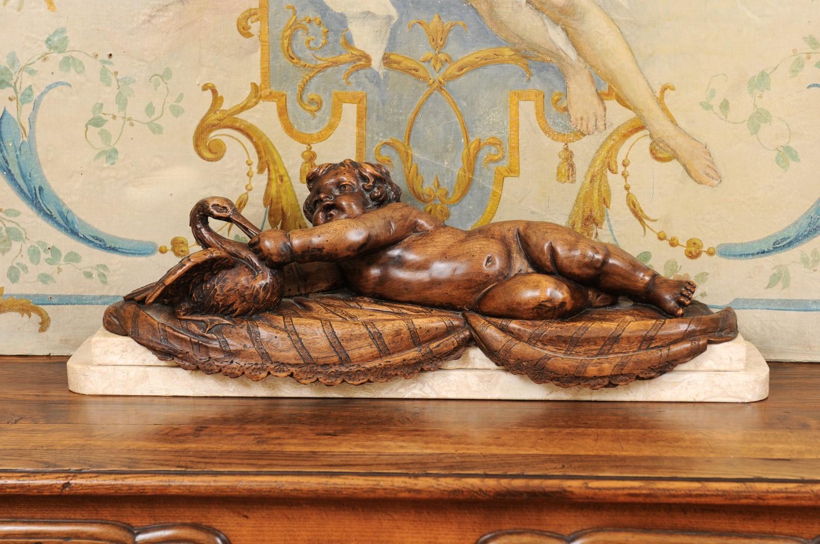 A French carved walnut putto feeding a swan sculpture from the late 19th century, with marble base. Created in France during the last quarter of the 19th century, this walnut sculpted group features a chubby putto laying on his side and extending