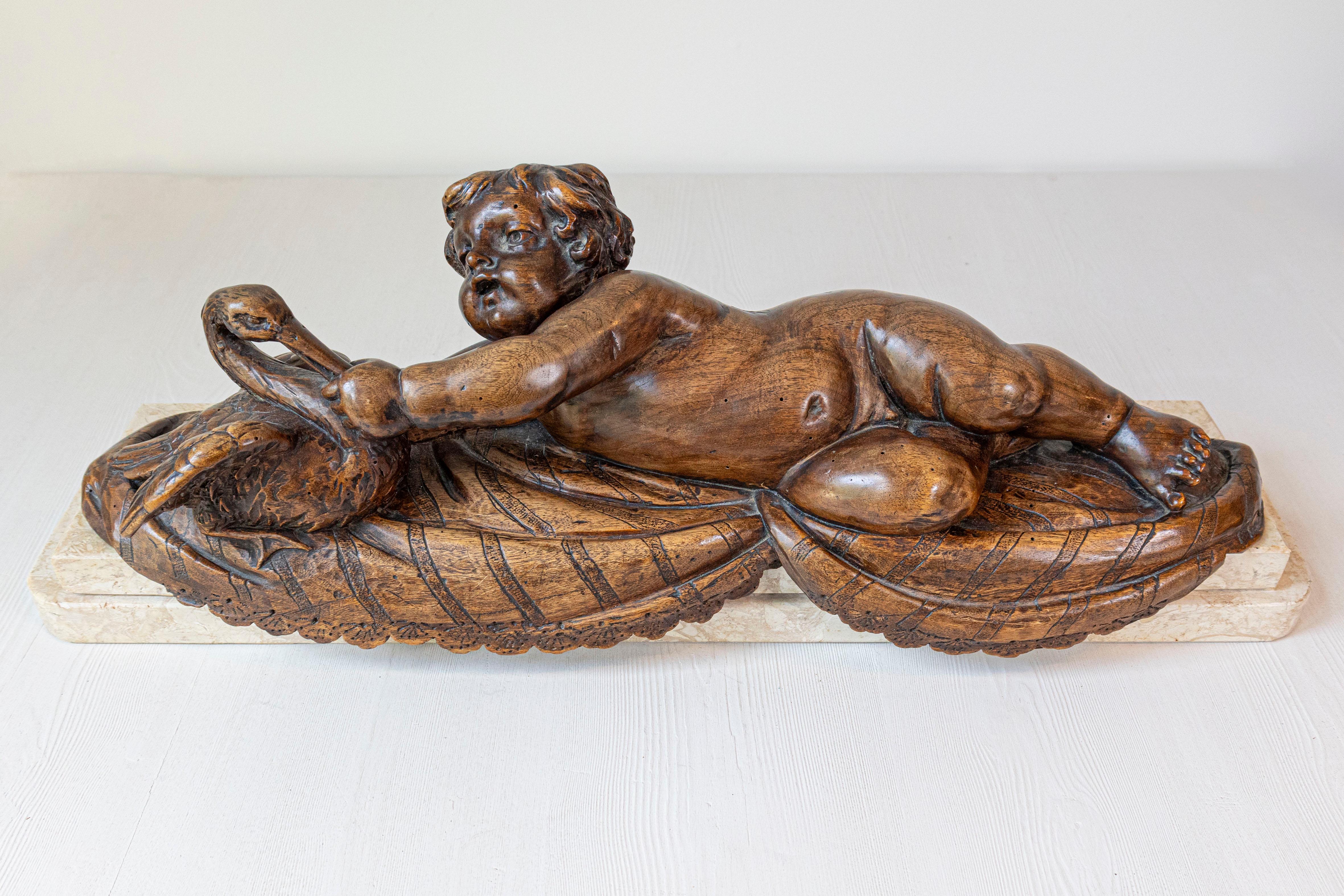 Putto francese intagliato in noce che nutre un cigno, scultura della fine del XIX secolo con base in marmo. Creato in Francia durante l'ultimo quarto del XIX secolo, questo gruppo scolpito in noce presenta un putto paffuto che si sdraia su un fianco