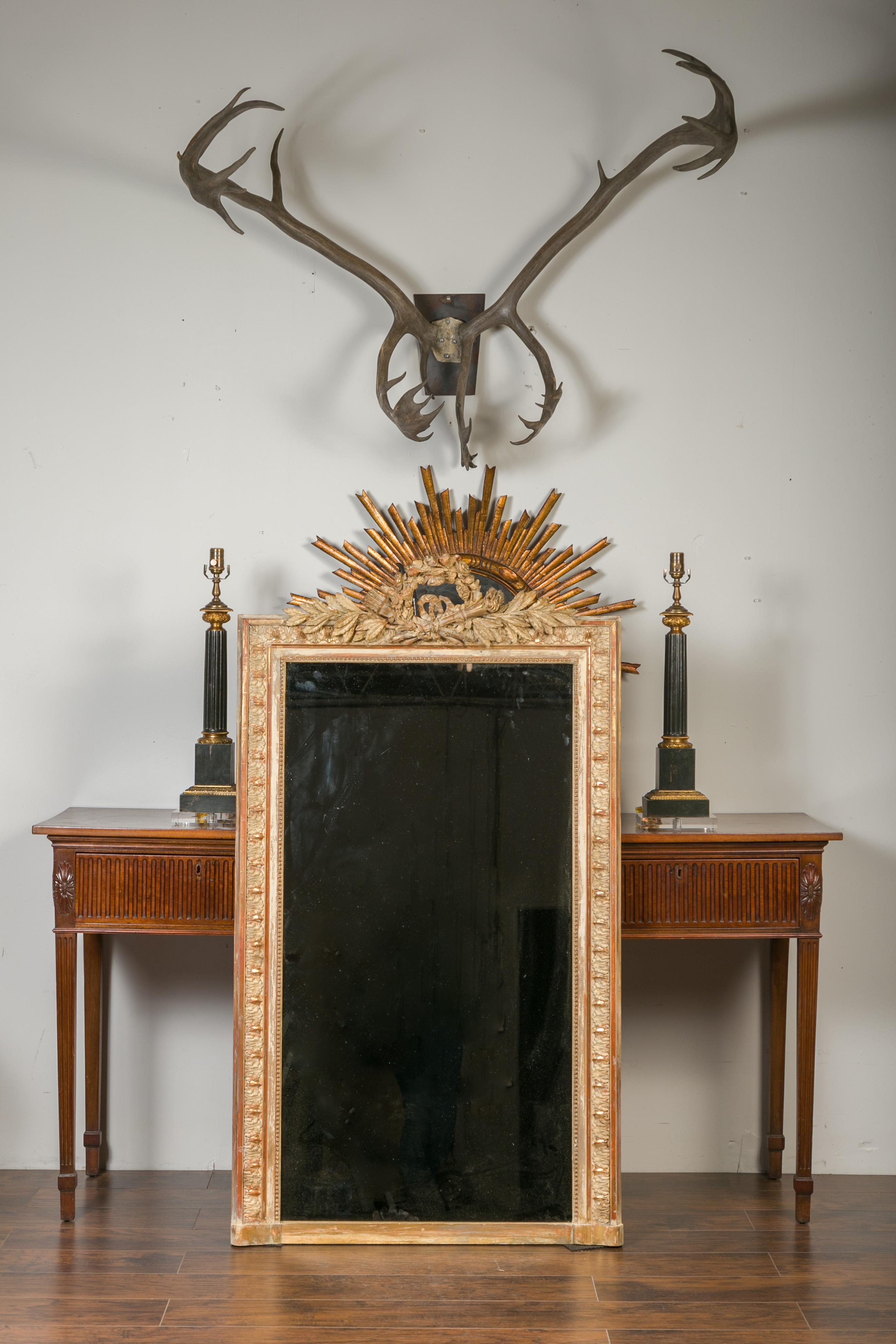 A French gilt and painted carved wooden mirror from the late 19th century, with floral wreath, torch and quiver motifs. Born in France during the last quarter of the 19th century, this tall mirror features an eye-catching crest adorned with a carved