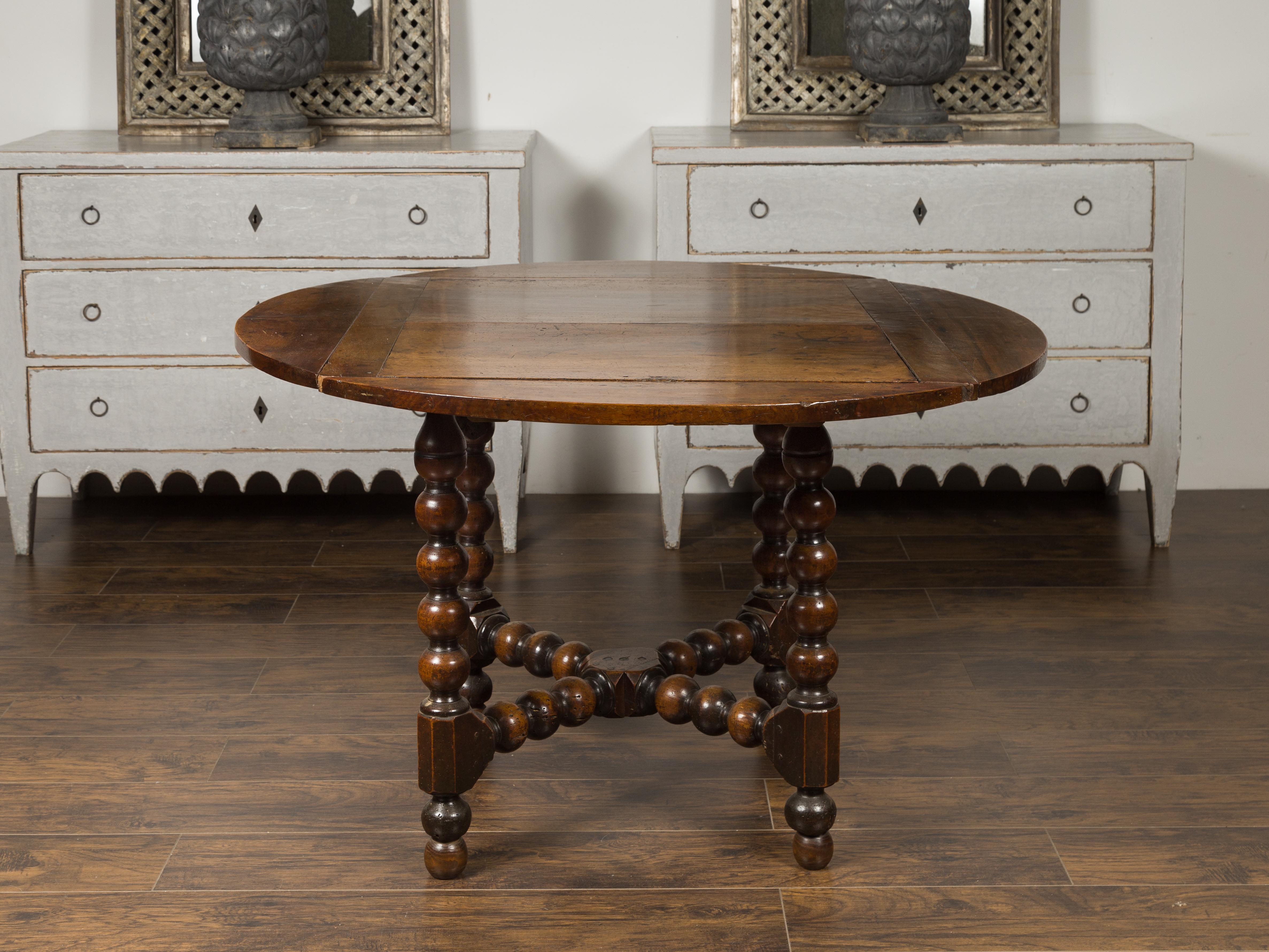 A French Louis XIII style walnut table from the late 19th century, with bobbin legs and cross stretcher. Born in France during the last quarter of the 19th century, this dining table features a circular planked top sitting above four bobbing legs