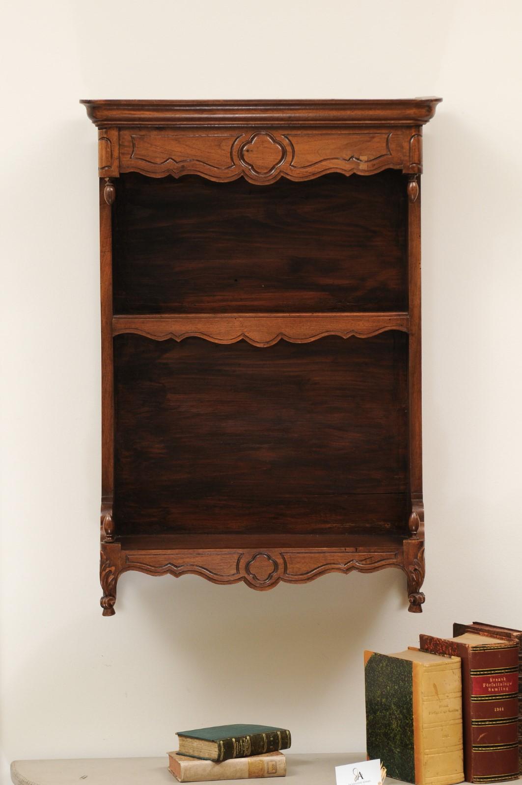A French Louis XV style late 19th century walnut rack from Provence with carved motifs and scrolling feet. Created in Southern France during the last quarter of the 19th century, this Provençal walnut wall rack features a molded cornice resting on a