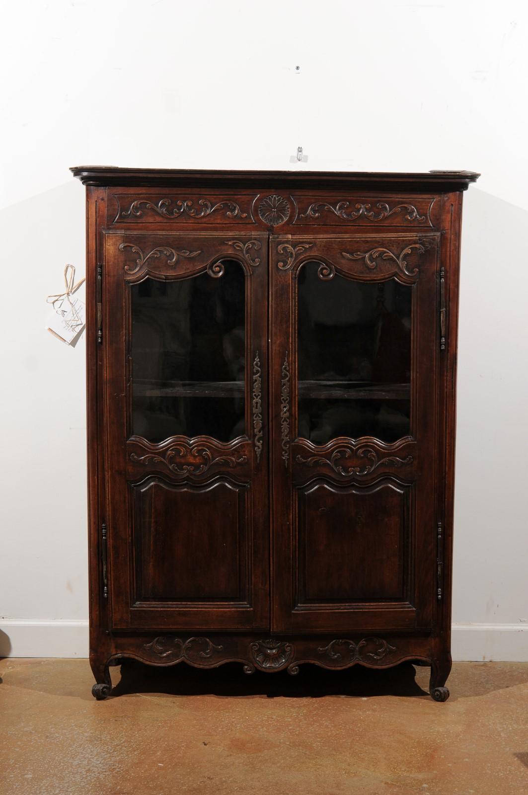 A petite French Louis XV style walnut vitrine from the late 19th century, with carved motifs and glass doors. Created in France during the last quarter of the 19th century, this walnut vitrine features a molded cornice sitting above two doors