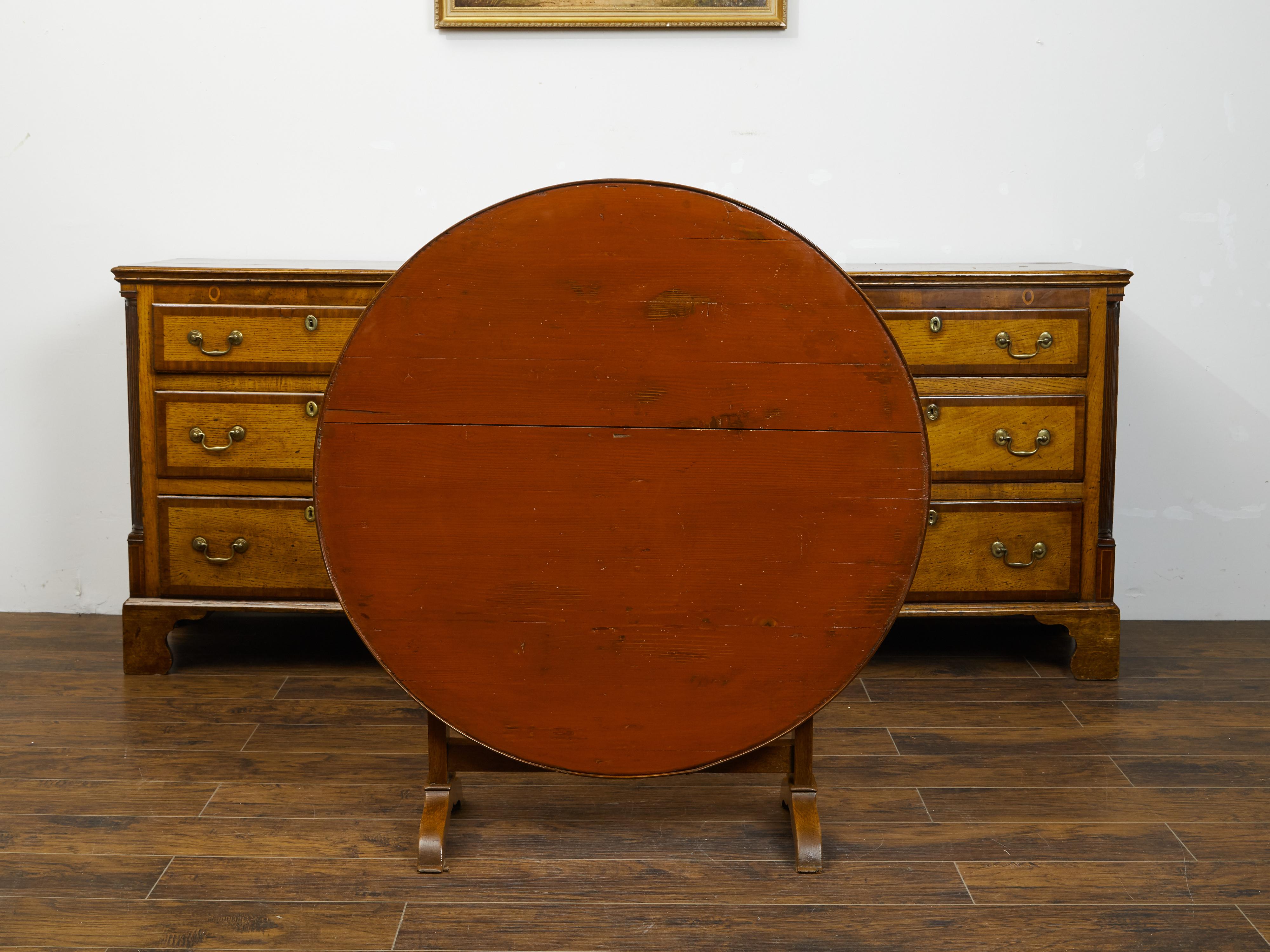 A French painted wood wine tasting table from the late 19th century, with circular top, trestle base and wedge. Created in France during the last quarter of the 19th century, this painted wine tasting table features a round planked tilt-top, sitting
