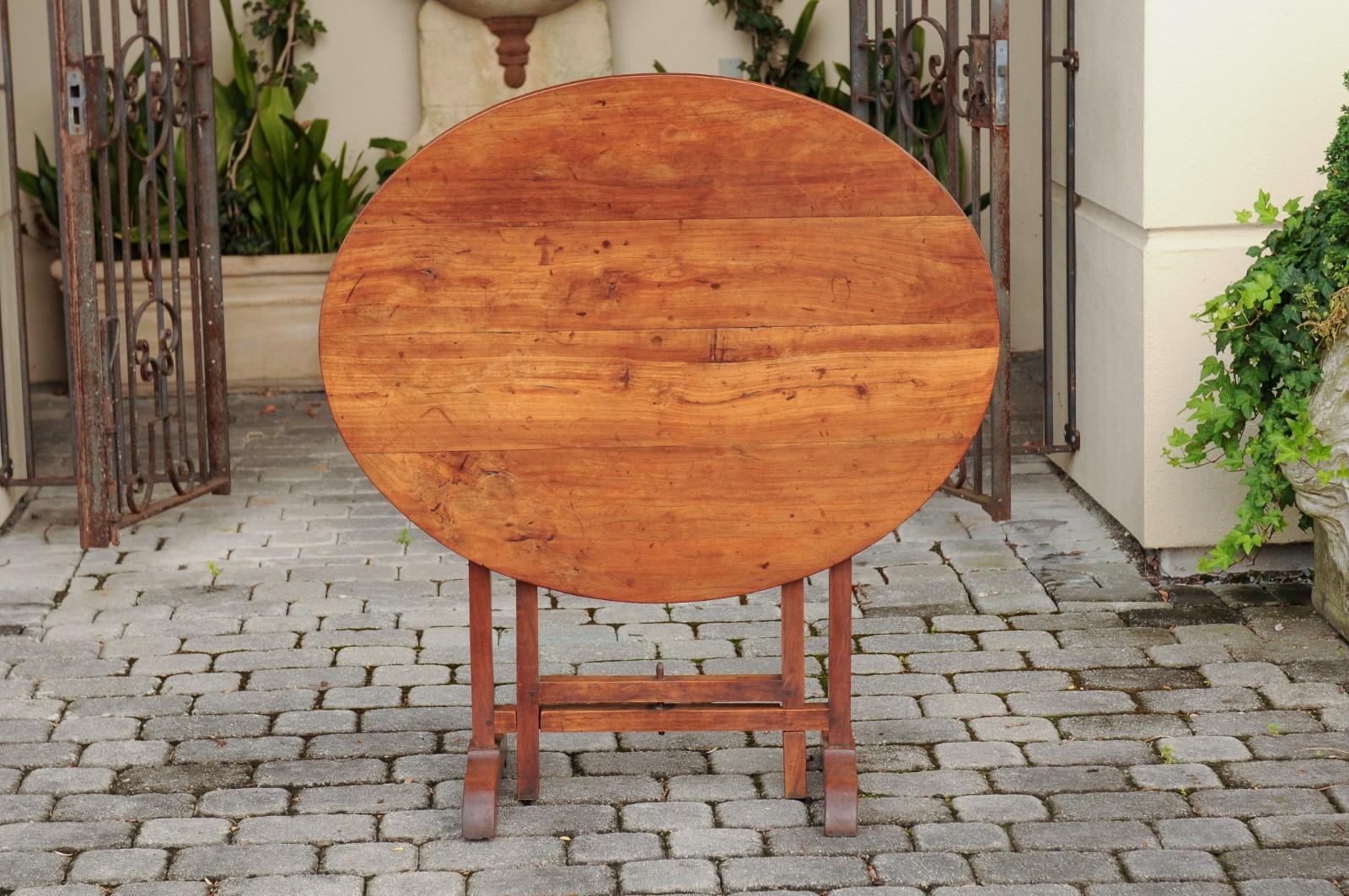 A French fruitwood wine tasting table from the late 19th century, with oval top and trestle base. Born in France during the later years of the politically dynamic 19th century, this fruitwood wine tasting table features an oval planked tilt-top ,