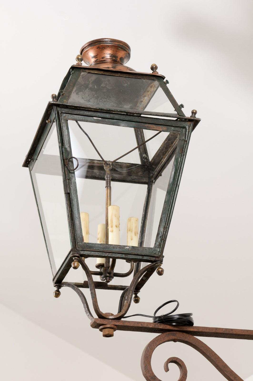 A French iron wall lantern from the late 19th century, with four lights, glass panels, and scrolling bracket. Created in France during the last decade of the 19th century at a time when the Impressionist roamed the countryside in search of