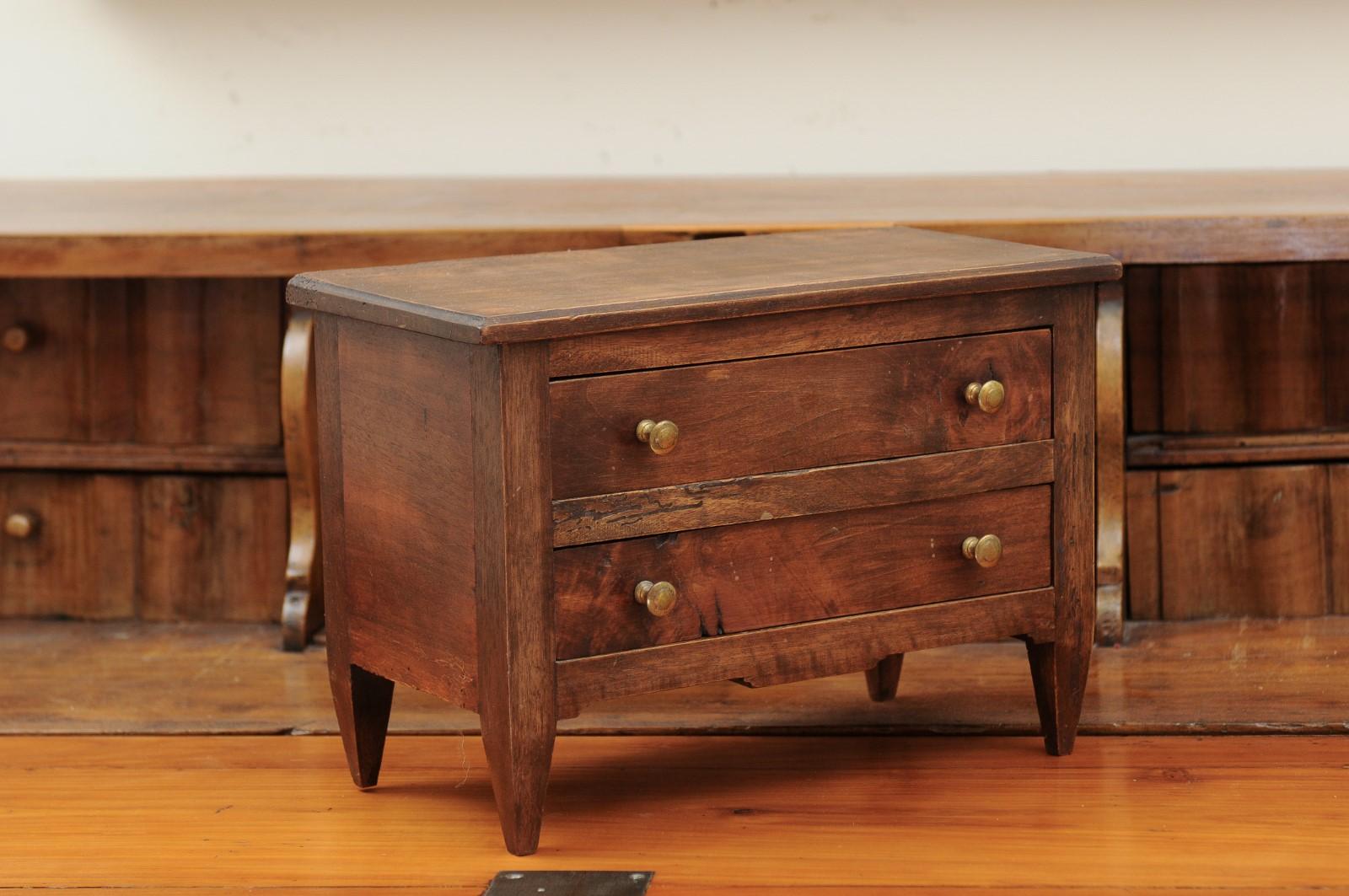 A French miniature walnut chest from the late 19th century with two drawers and tapered legs. Created in France during the last decade of the 19th century likely to be a salesman sample, this miniature chest features a rectangular top sitting above
