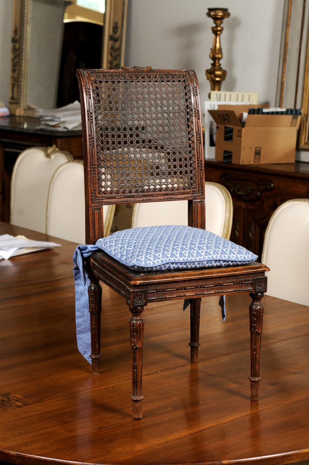 A French walnut child's chair from the late 19th century, with cane seat and upholstered cushion. Created in France during the last decade of the 19th century, this petite walnut chair features an out-scrolling cane back with carved motifs on the