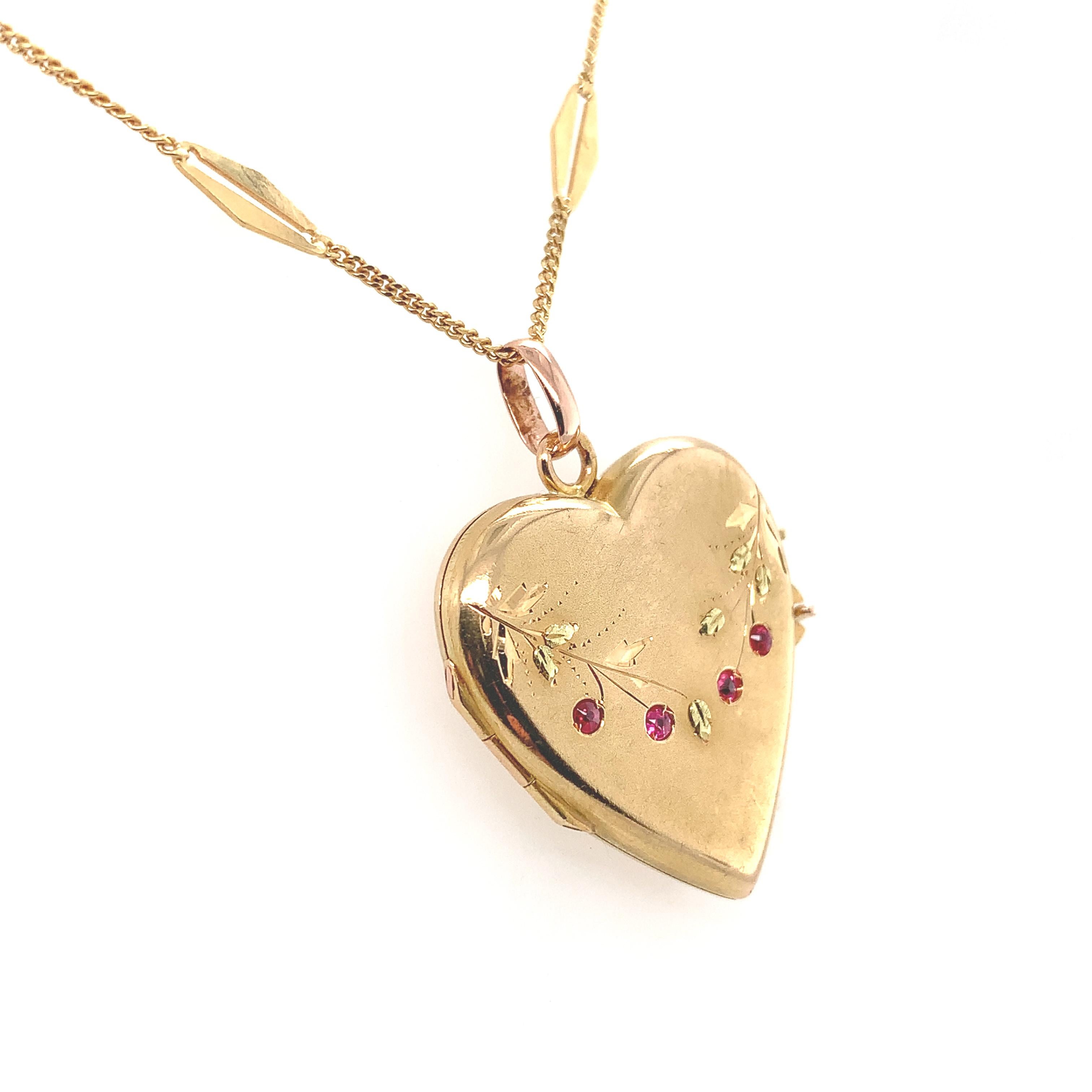 18K yellow gold heart shaped locket with applied green gold leaves and 4 small synthetic ruby accents. There is a French eagle hallmark on the loop attached to the heart. The heart also has engraved leaves and branches. The synthetic rubies each