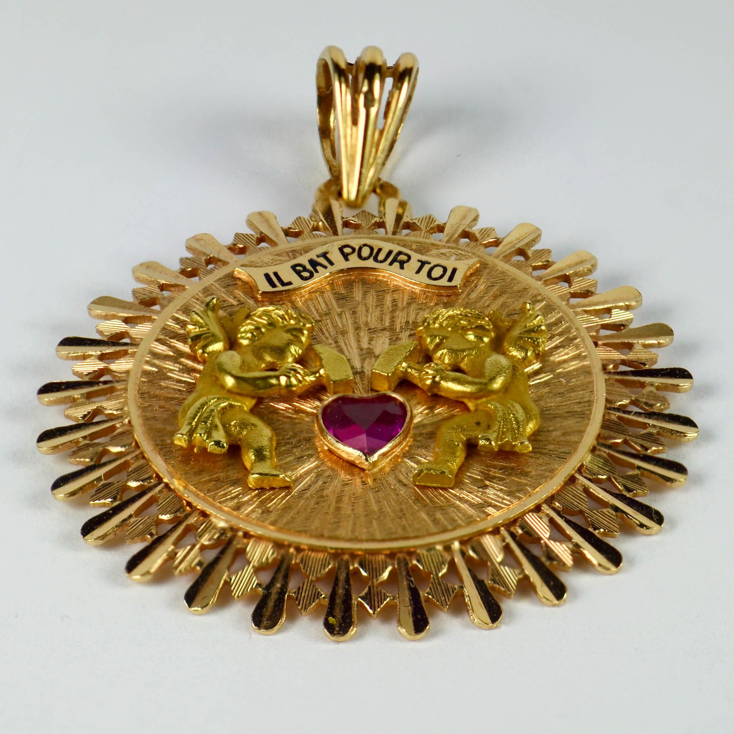 A French 18 karat (18K) rose gold charm pendant designed as a rose gold sunburst textured disk with two mechanical yellow gold cupid figures with hammers taking it in turns to hit the ruby love heart. Above them a enamelled scroll reads 'Il bat pour