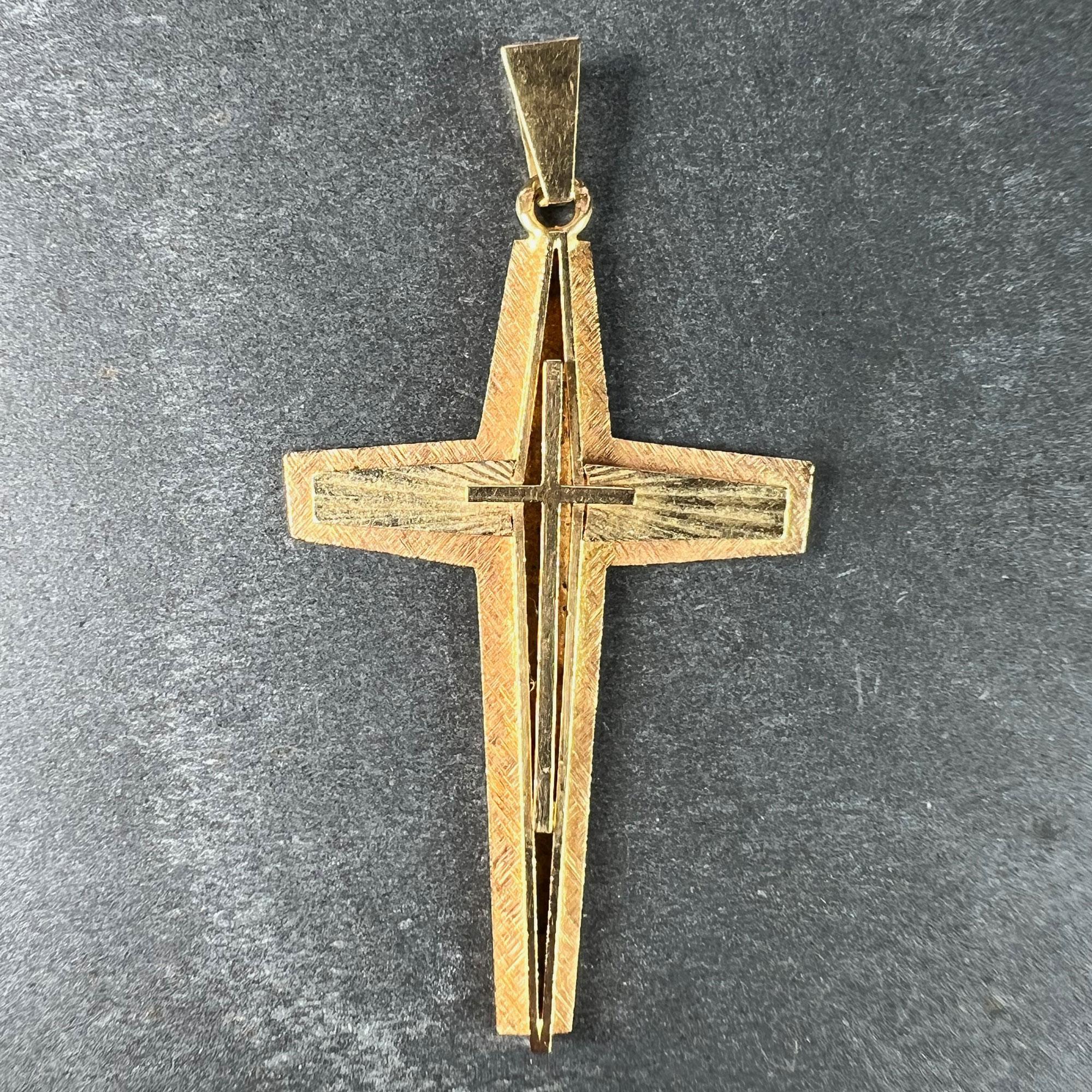 A French 18 karat (18K) yellow gold pendant designed as a cross with three layers. The base layer with a cross-hatched textured surface. The second layer is raised and hollow to the vertical, with a radiating pattern to the horizontal arms. The