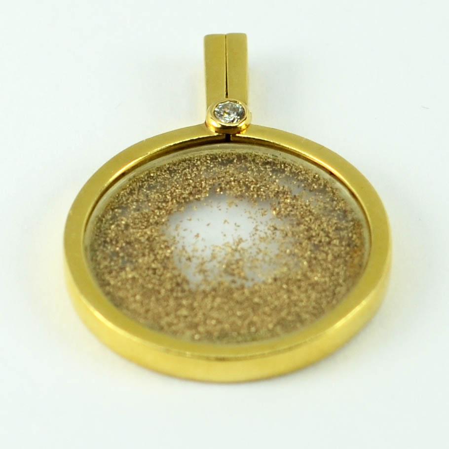 A French 18 karat (18K) yellow gold pendant designed as a glass lens enclosing gold dust, further embellished with a round brilliant cut diamond estimated to weigh approximately 0.10 carats. Stamped with the eagle’s head punch mark for 18 karat gold