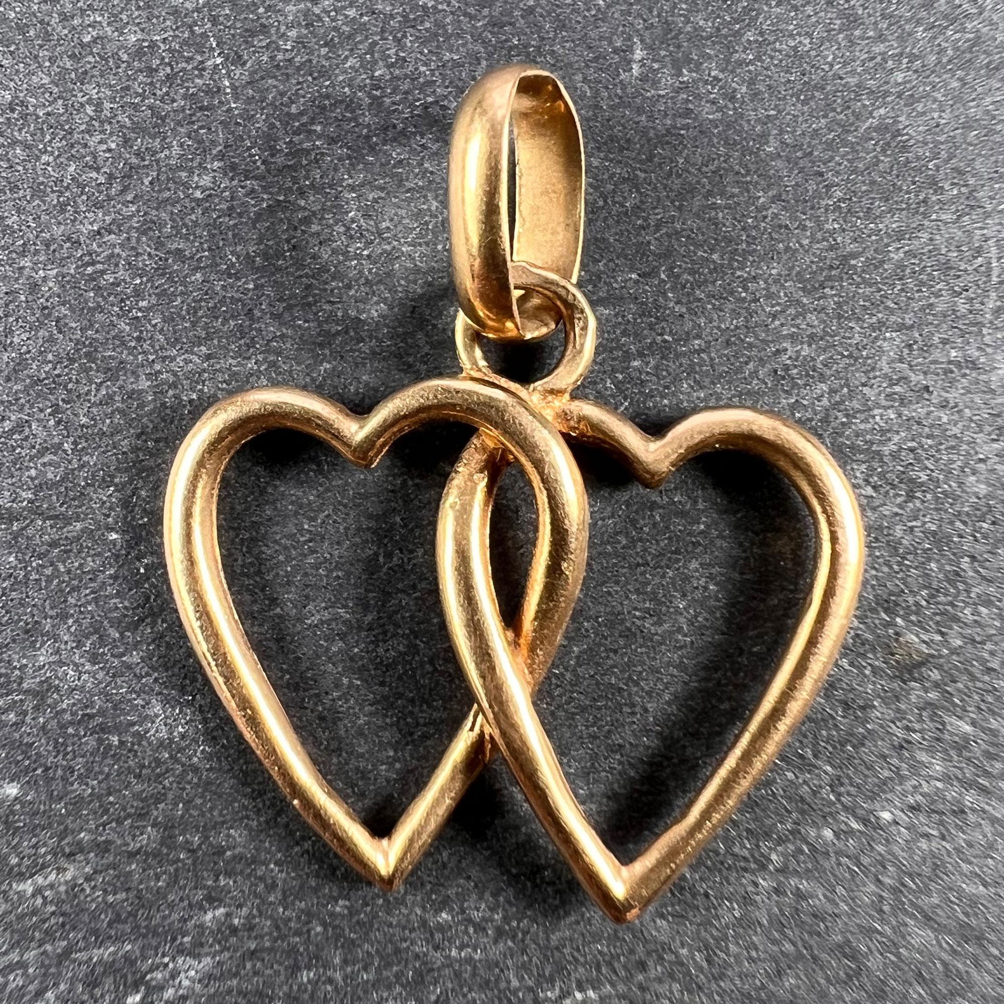 An 18 karat (18K) yellow gold charm pendant designed as a pair of entwined love hearts. Stamped with the eagle's head for 18 karat gold and French manufacture, along with an unknown maker's mark.

Dimensions: 1.5 x 1.7 x 0.2 cm (not including jump