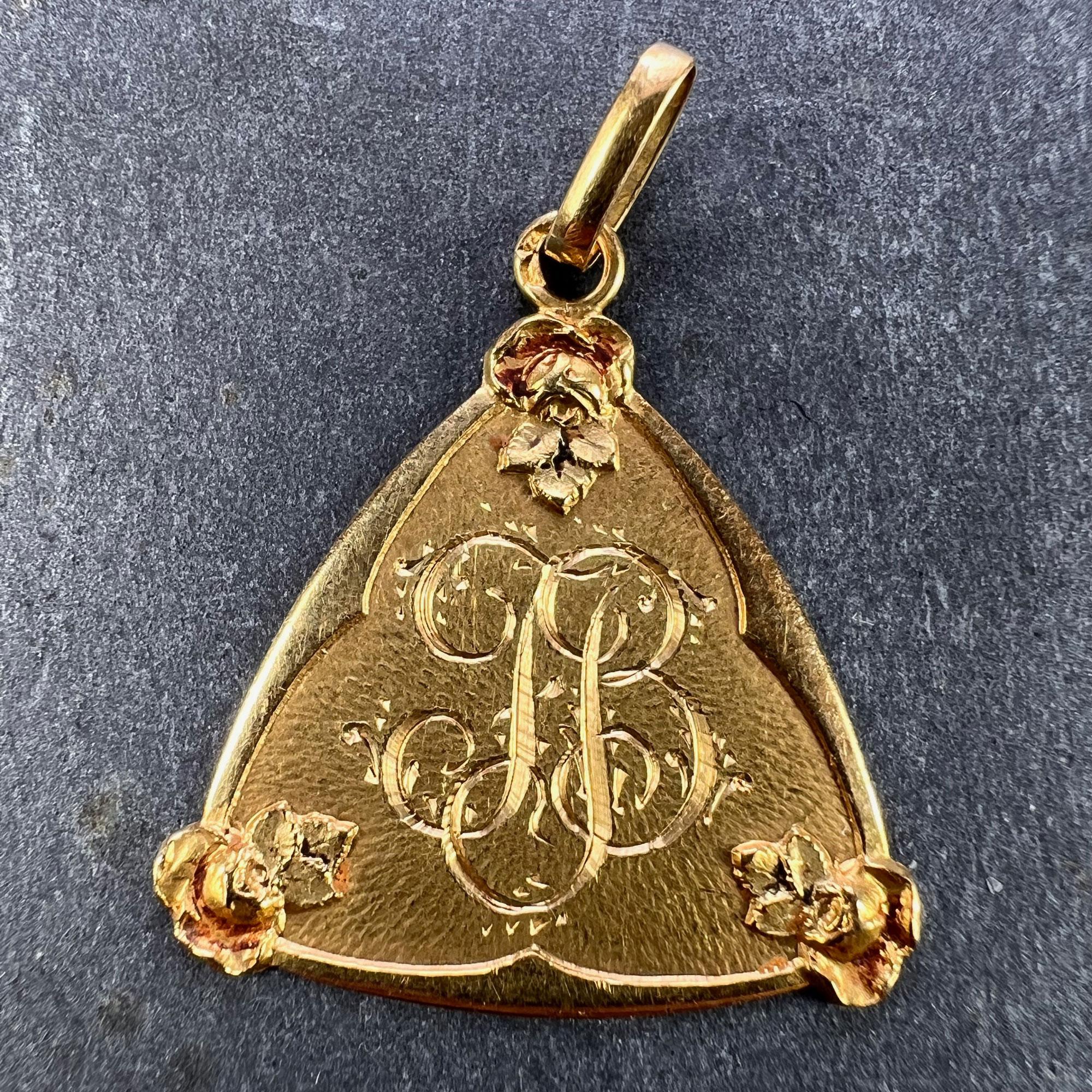 A French 18 karat (18K) yellow gold charm pendant designed as an triangular medal detailing a monogram with the initials JB in engraved script within a triangle framed by roses and rose leaves. Engraved to the reverse with the date '3 Novembre