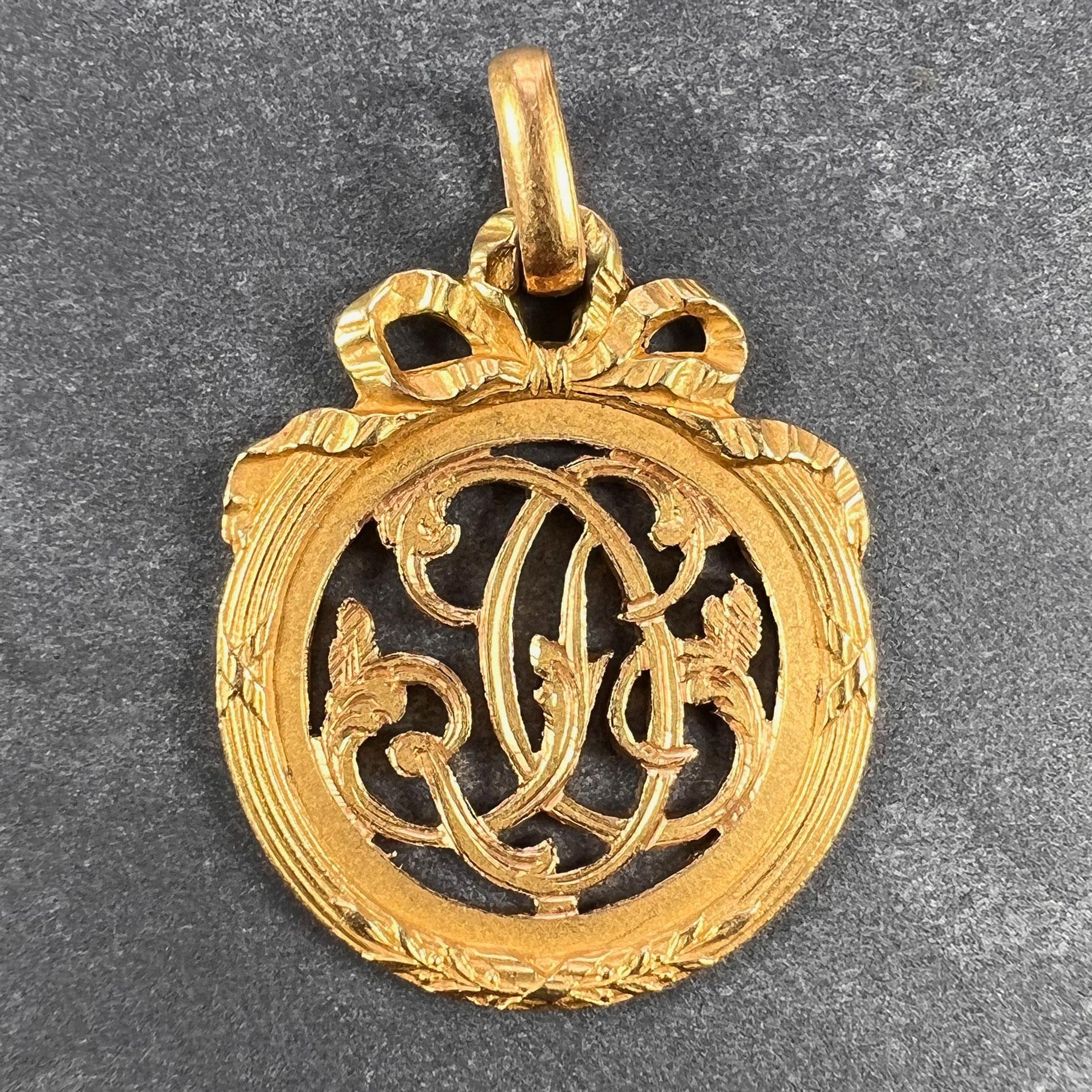 A French 18 karat (18K) yellow gold charm pendant  designed as a medal with a reeded border entwined with ribbons and surmounted with a bow, detailing the monogram DC. Stamped with the eagle mark for 18 karat gold and French