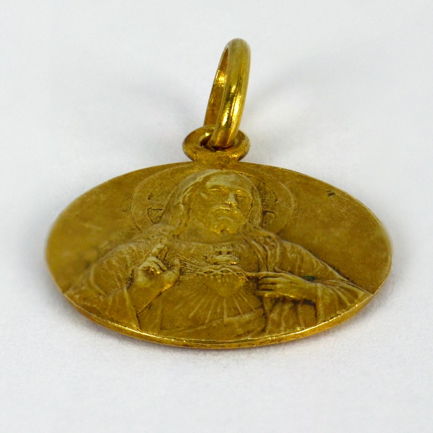 A French 18 karat (18K) yellow gold charm pendant designed as a round medal depicting Jesus with a Sacred Heart to one side, the other depicting the Basilique du Sacre Coeur in Montmartre. Stamped with the eagle’s head for 18 karat gold and French