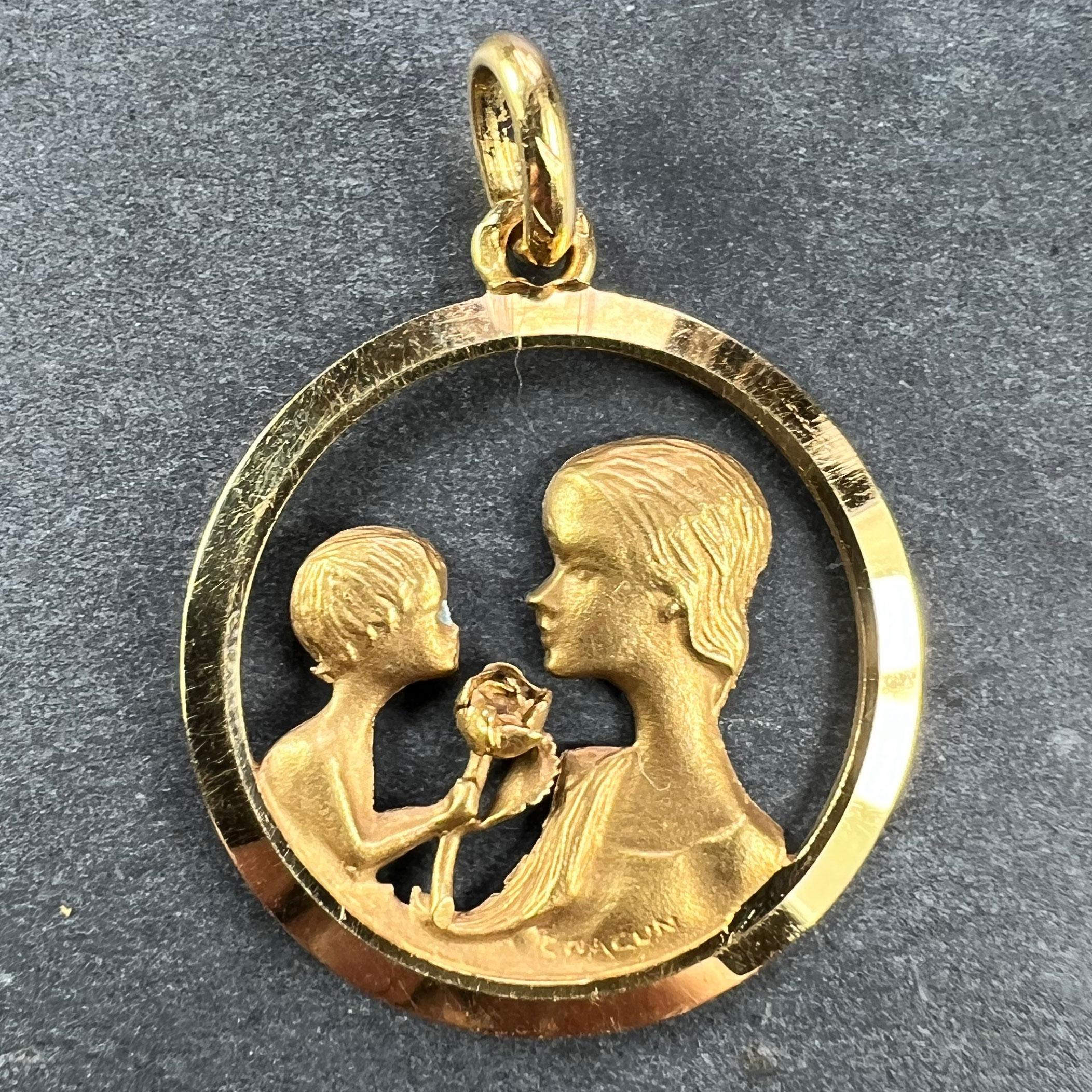 A French 18 karat (18K) yellow gold charm pendant designed as a round medal pierced with a sculpted relief of a Mother and Child, with the child offering the mother a rose. Stamped with the eagle's head for minimum 18 karat gold and French