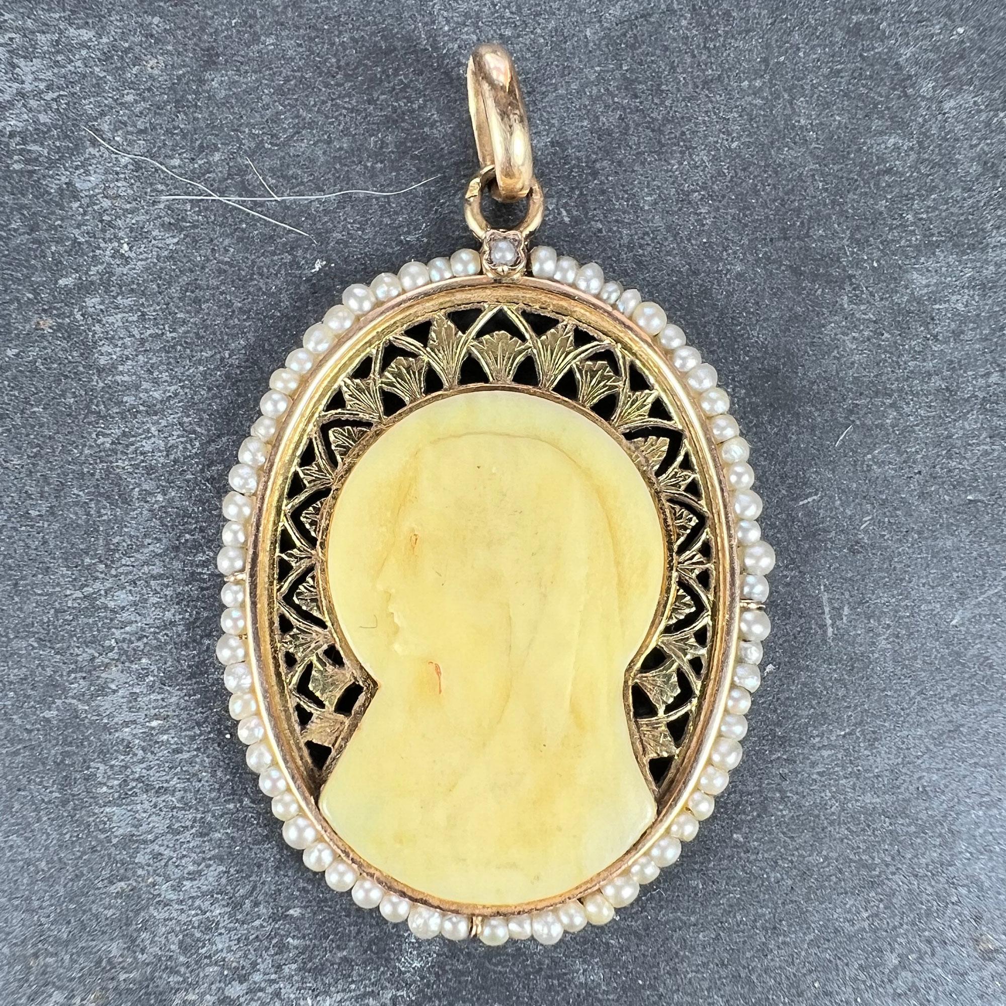 A French 18 karat (18K) yellow gold charm pendant designed as an oval representing the Virgin Mary as a Bakelite cameo set in a pierced frame, surrounded by 66 natural white seed pearls with a single seed pearl collet set to the top. Stamped with