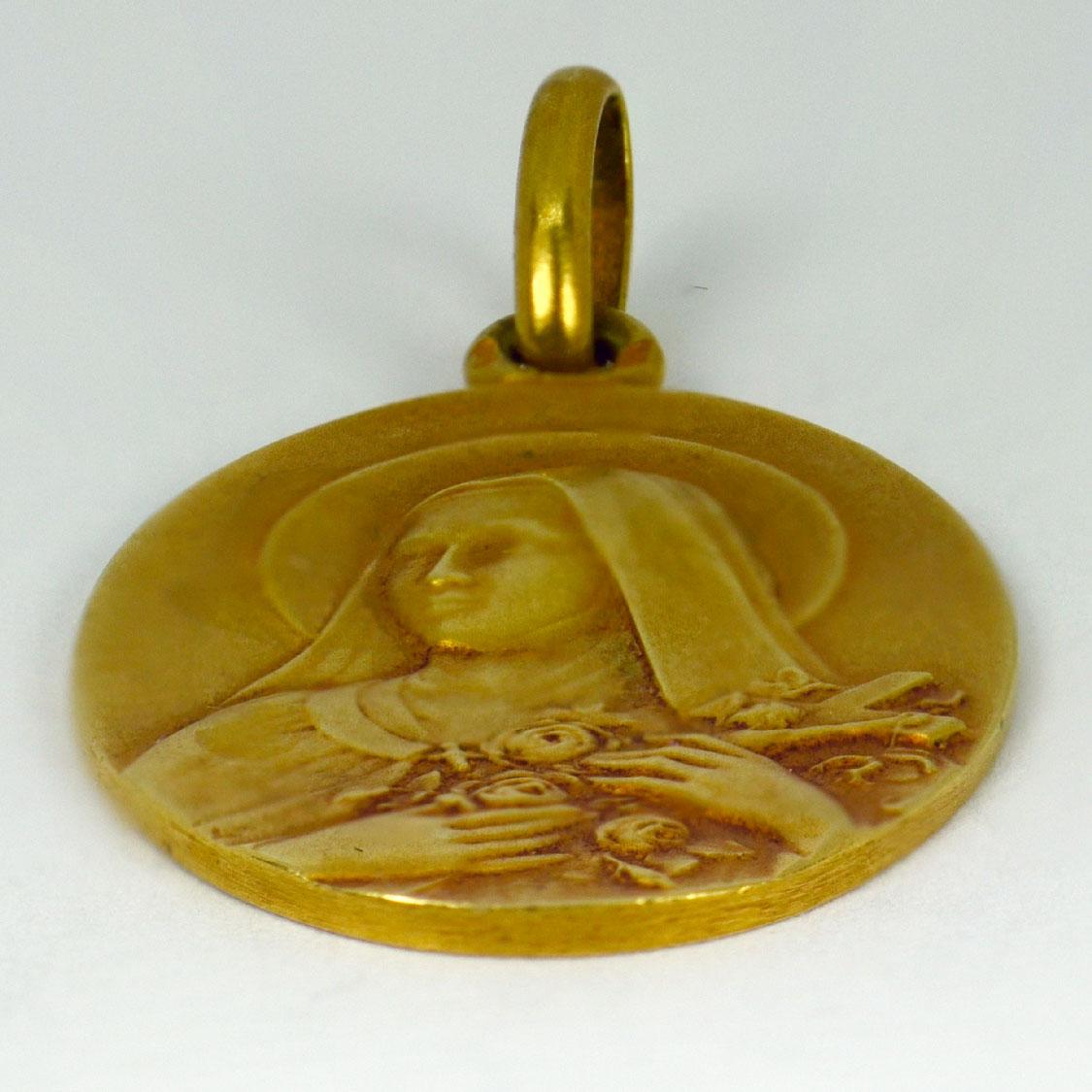 A French 18 karat (18K) yellow gold charm pendant designed as an oval medal depicting St Therese holding a crucifix within a sheaf of roses. Stamped with the eagles head for French manufacture and 18 karat gold with an unknown maker’s