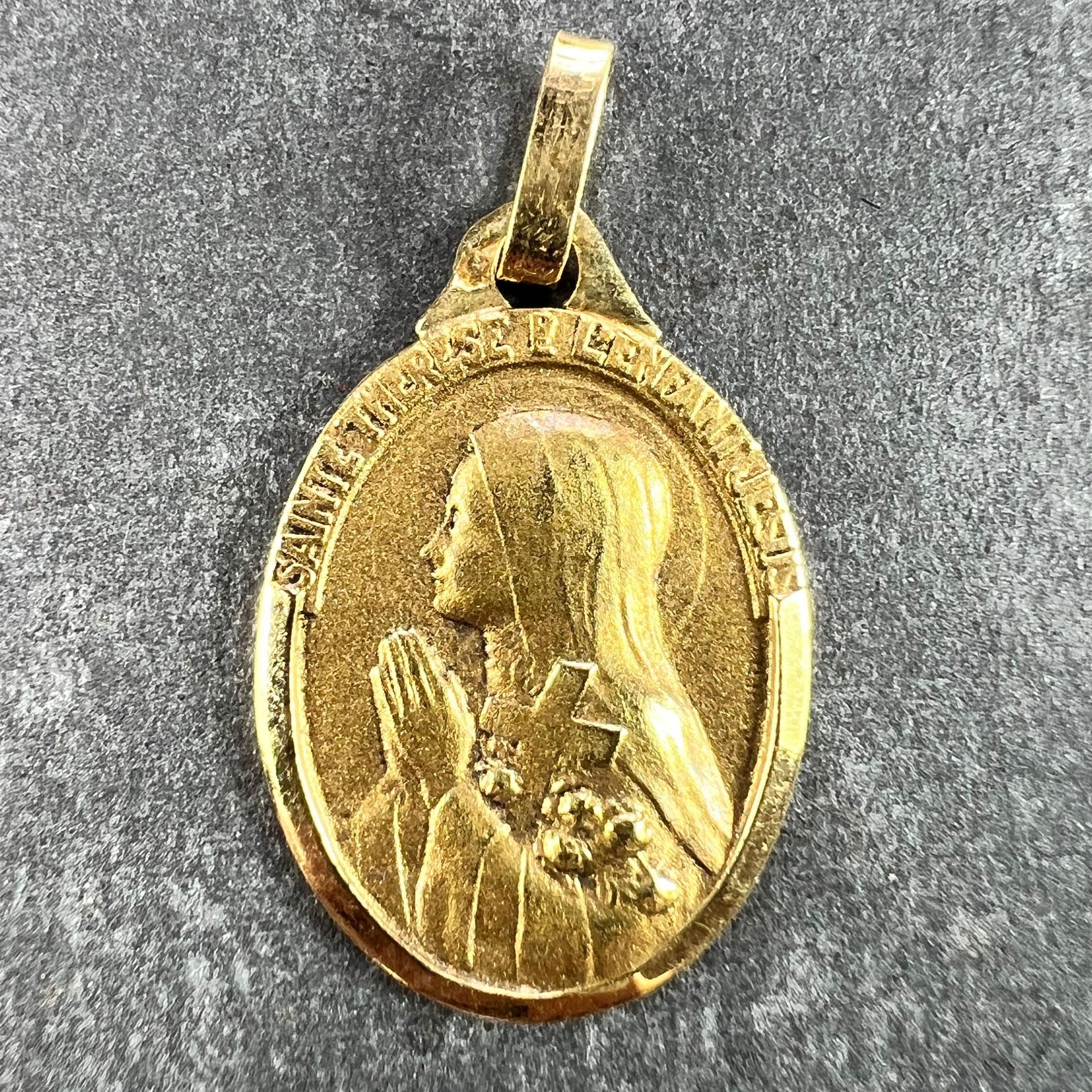 Colgante francés de oro amarillo de 18 quilates (18K) diseñado como una medalla ovalada que representa a Santa Teresa sosteniendo un crucifijo y unas rosas con un contorno pulido. El reverso muestra una corona de rosas que rodea una cruz. Sello con