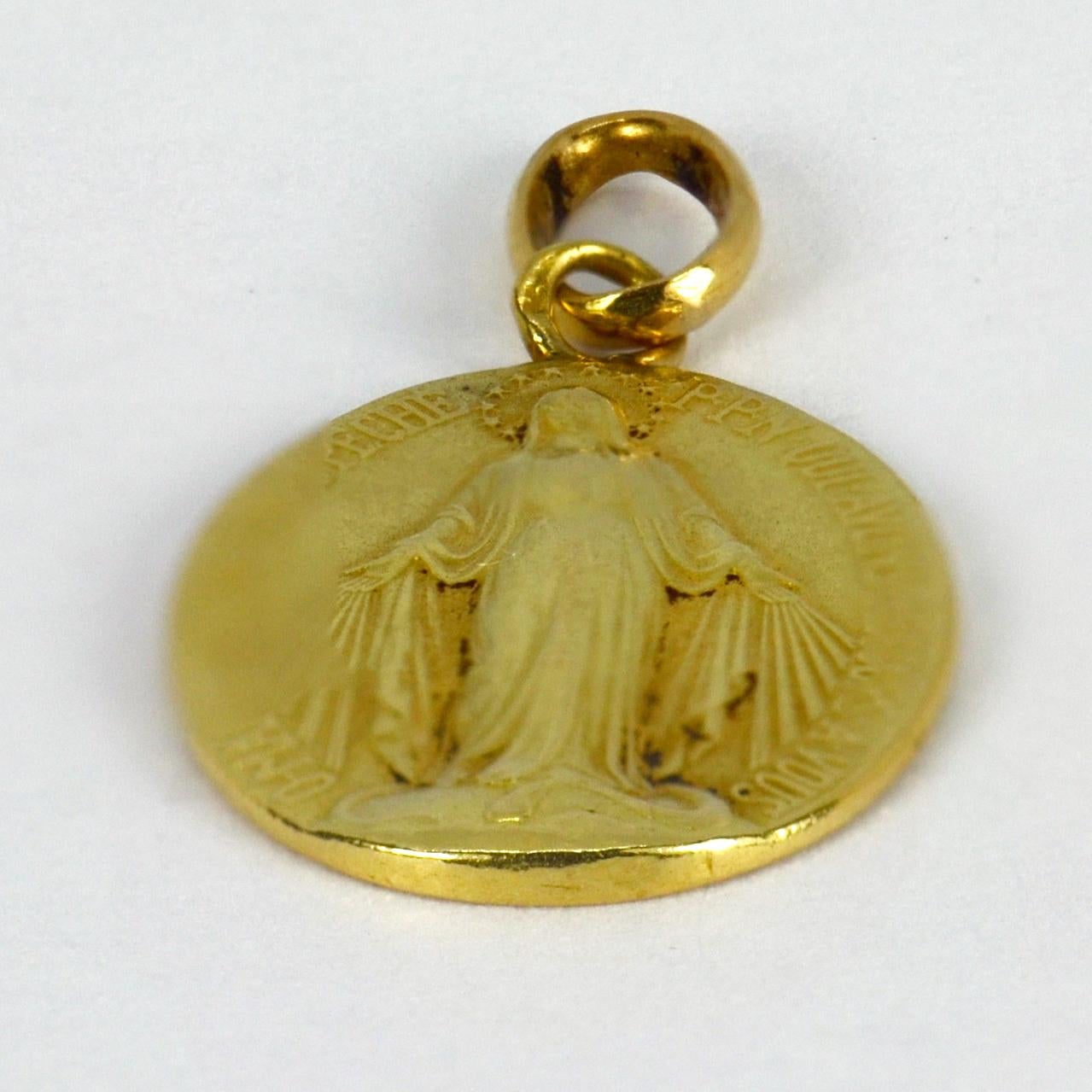 A French 18 karat (18K) yellow gold charm pendant designed as the Miraculous Medal. The medal depicts the Virgin Mary standing on a globe, crushing a serpent beneath her feet with rays shooting from her hands to symbolise the graces she bestows on