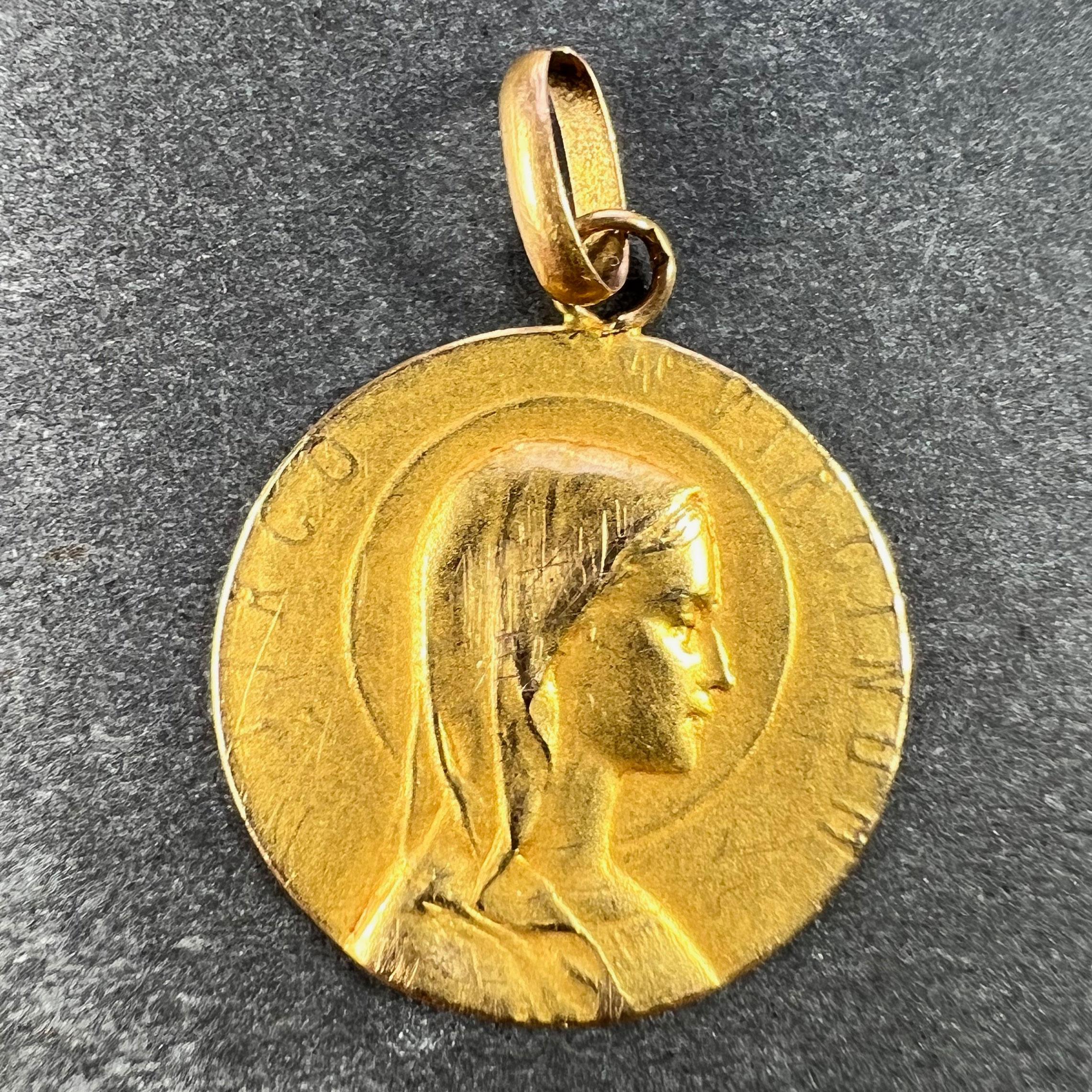A French 18 karat (18K) yellow gold charm pendant designed as a round medal with a relief of the Virgin Mary in profile with a halo, with the Latin motto 'VIRGO VIRGINUM' (Virgin of Virgins) surrounding. The reverse depicts a book or bible with a
