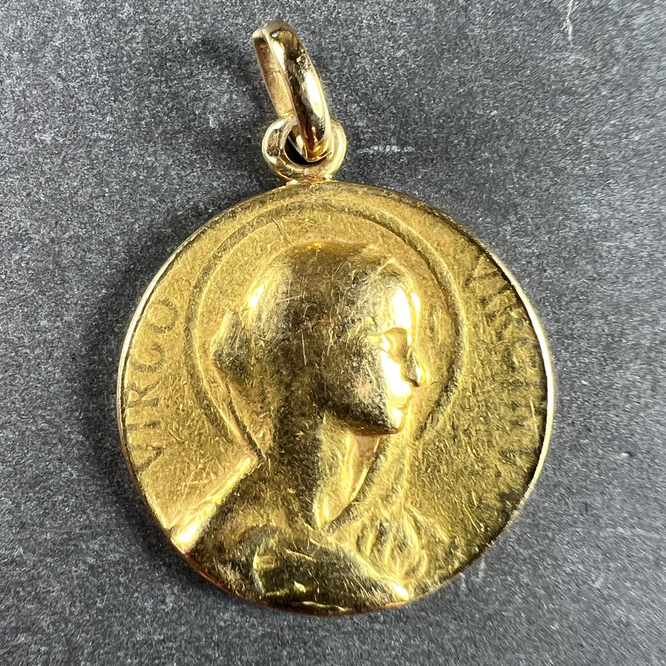A French 18 karat (18K) yellow gold charm pendant designed as a round medal with a relief of the Virgin Mary in profile with a halo, with the Latin motto 'VIRGO VIRGINUM' (Virgin of Virgins) surrounding. The reverse depicts the letter M on a cloud