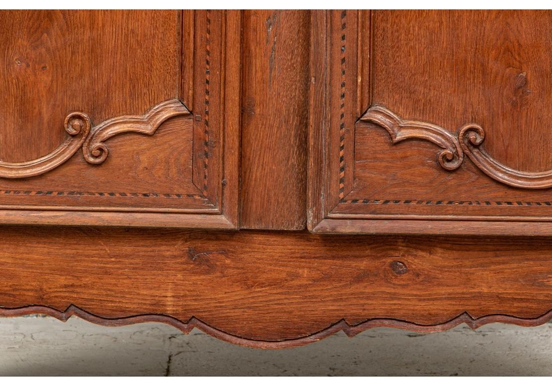 A fine authentic antique French cabinet with carved cornice over an inlaid panel with a cross and checked inlaid vines. The carved double doors with checked string inlaid borders. Fine metal hardware with escutcheon and a key. Two inside shelves