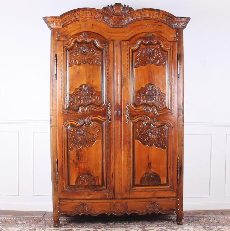 A Louis XV style 18th century cherry two-door armoire with an unusual double-arched profile. The panelled doors are profusely carved with flowers, swags etc., and open to reveal three shelves. Solid cherry panelled sides. There is ample depth for