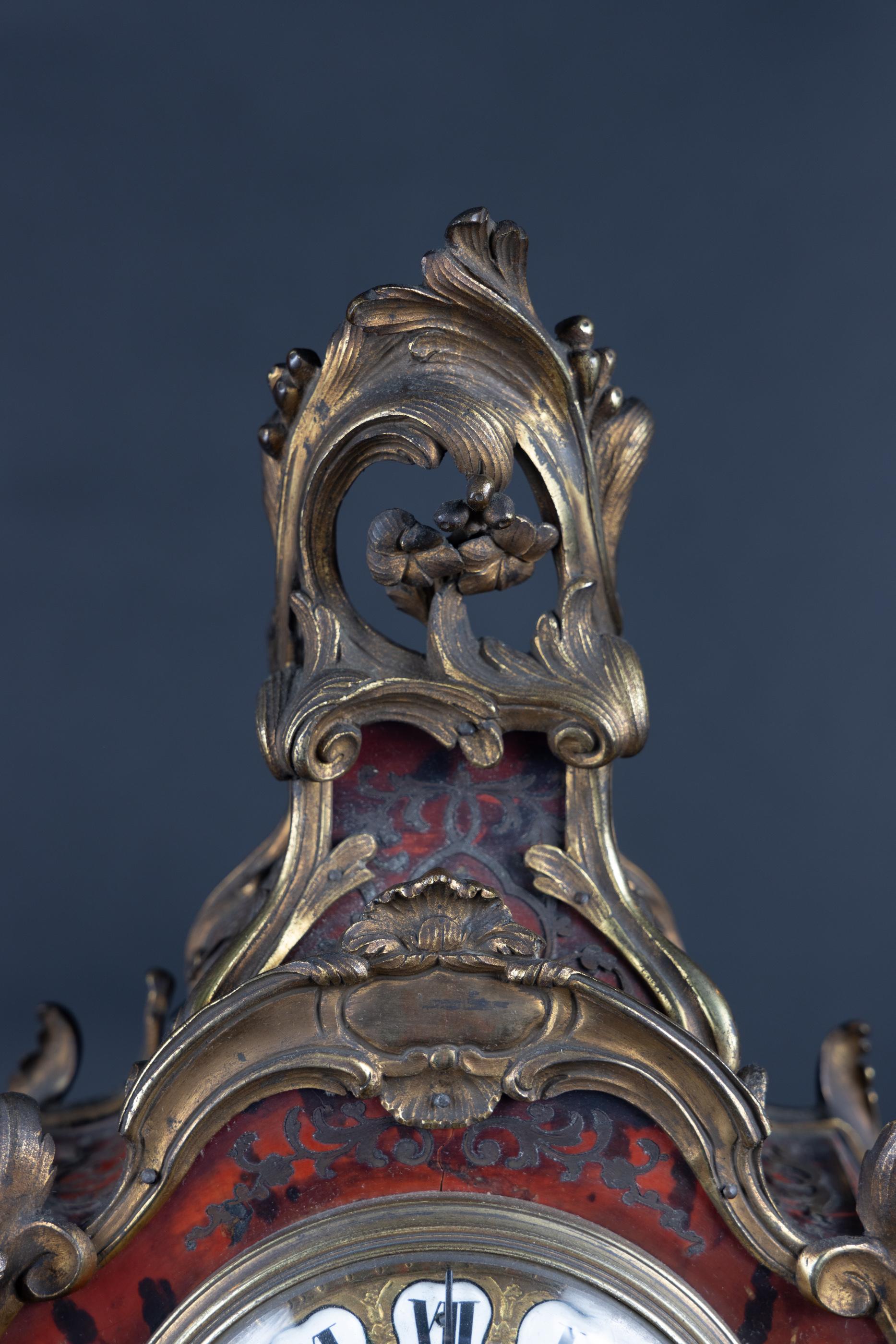 French 18th century Boulle clock on Boulle stand. The Louis XV clock has bronze mounts, with enameled Roman numerals for each hour.  The pendulum can be seen through a glass below the face.  On either side there is a decorative reticulated bronze. 