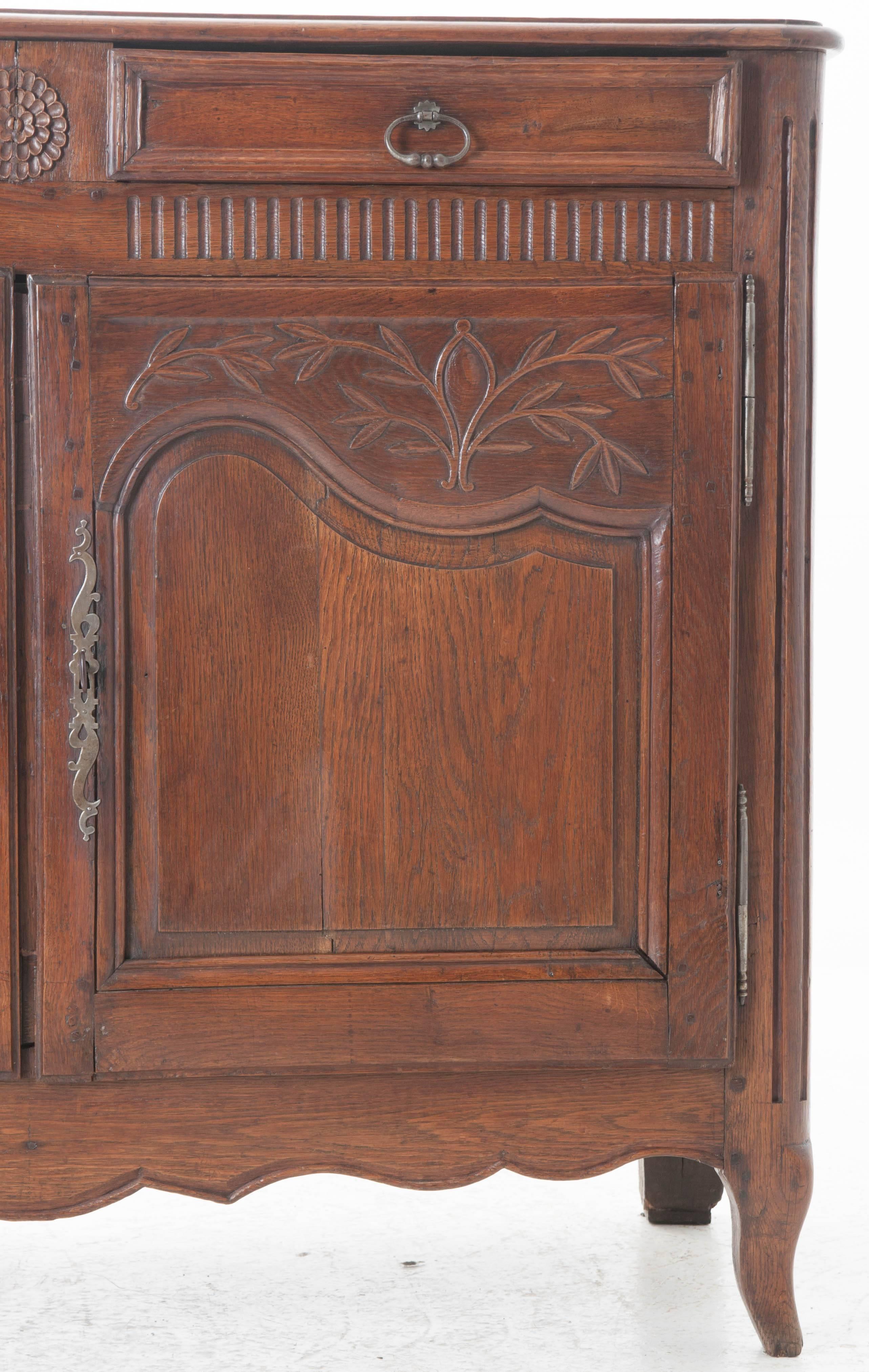 A fabulous 18th century French buffet constructed of brilliantly aged solid oak. Two drawers sporting their original pulls are separated from one another by a meticulously carved, radiating flower, and are separated from the doors they surmount by