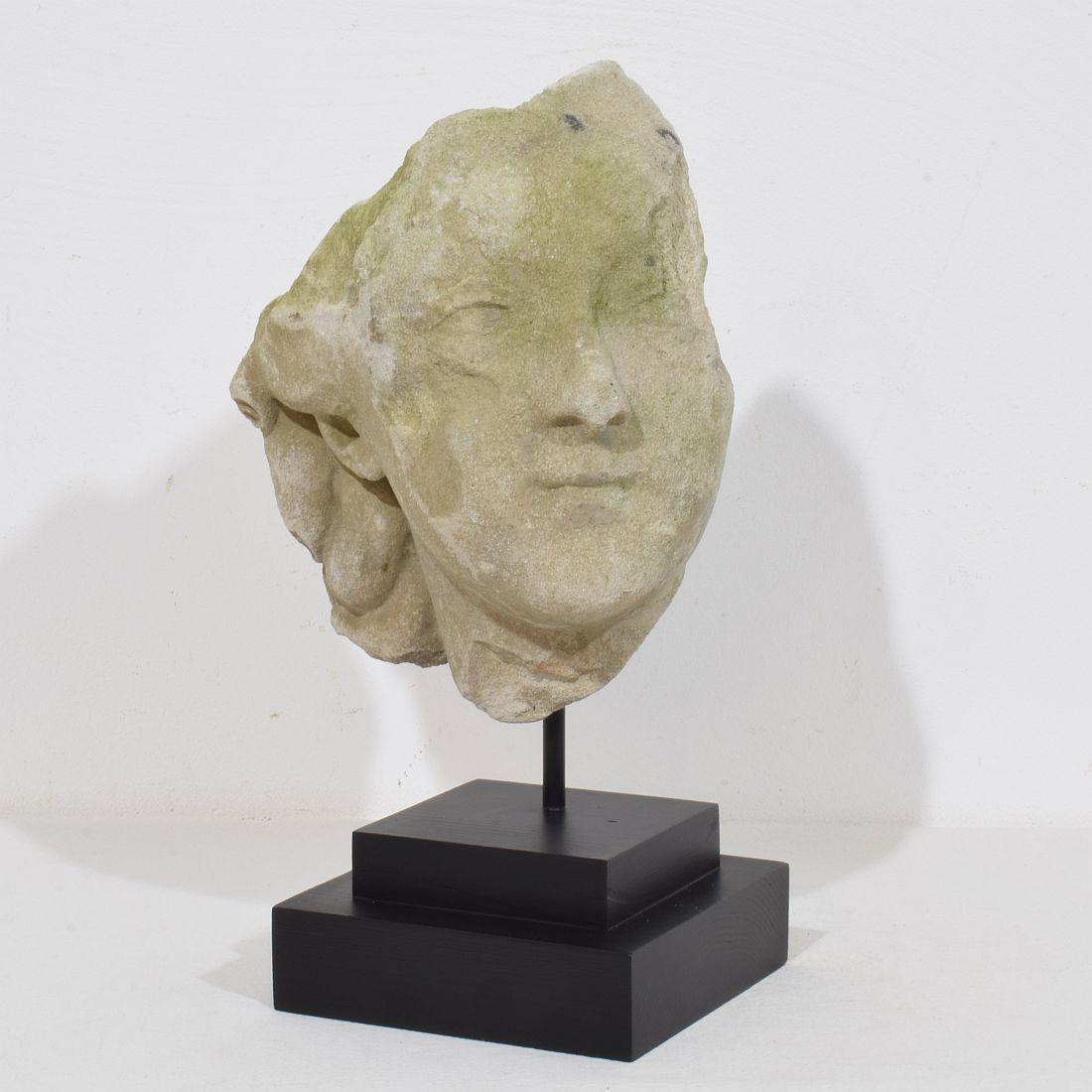 Magnificent carved stone head fragment with a very beautiful and strong expression.
France, circa 1750.
Beautiful weathered and small losses.
Measurement is with the wooden base.
H:32cm  W:20cm D:14cm 
