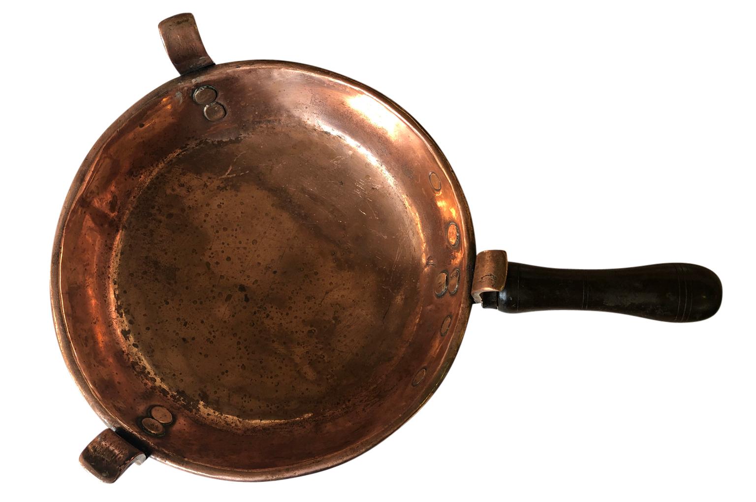 A very charming 18th century footed heavy gauge copper pan with wooden handle. A terrific accent piece for a kitchen island or living area.
