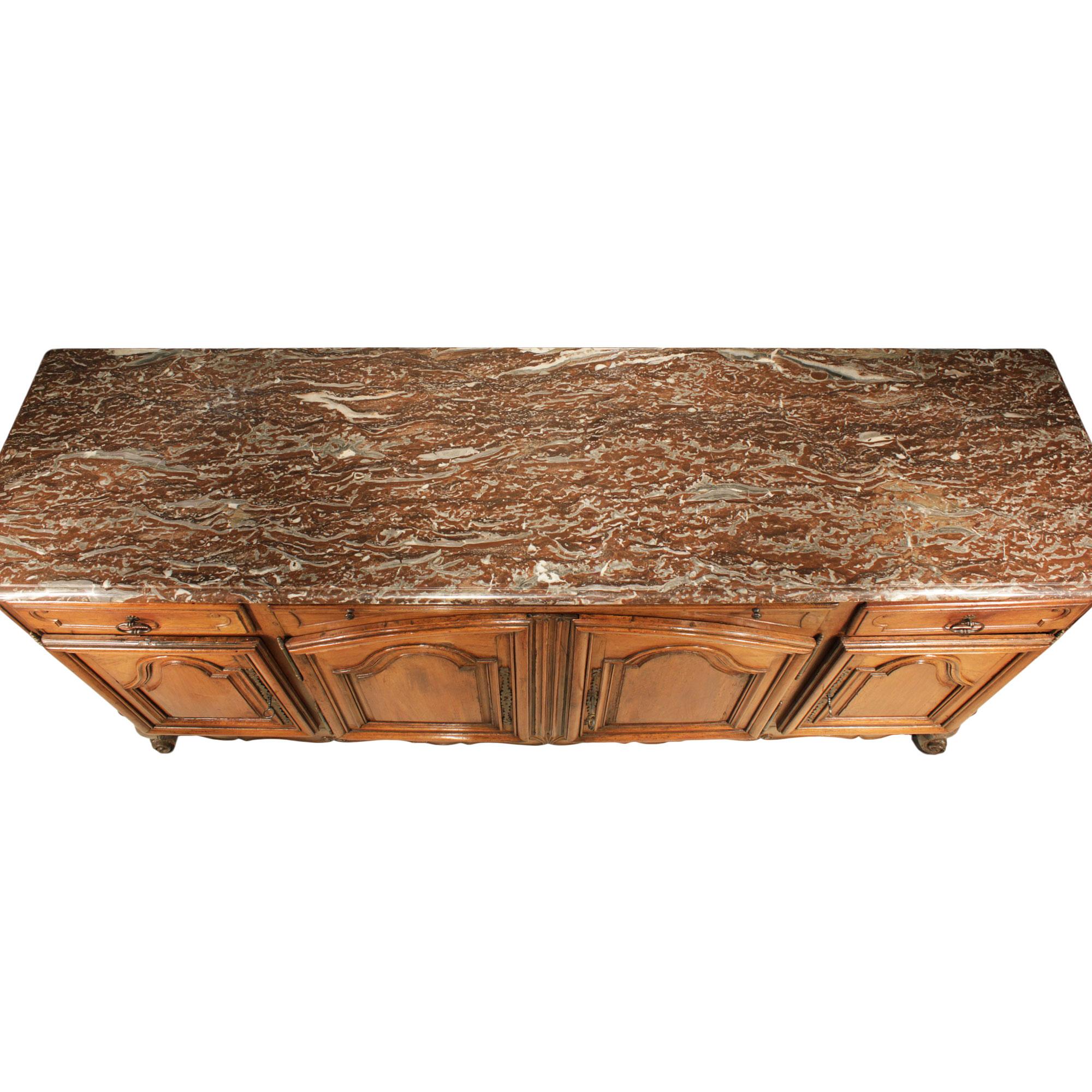 Un bel buffet in noce del XVIII secolo in stile Luigi XV. Il buffet sollevato da supporti Roqvillard presenta un elegante fregio smerlato con una conchiglia centrale intagliata. Sopra ci sono le quattro porte in noce massiccio screziato. La parte