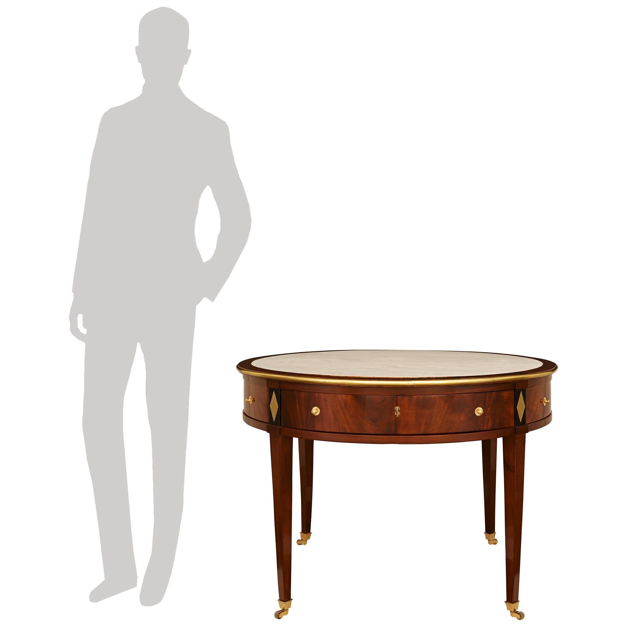 A handsome and most unique French late 18th century Directoire Period Flame Mahogany, Ebony, white Carrara marble and Ormolu center table. This wonderful circular table is raised on four square tapered Mahogany legs ending with Ormolu sabots and the