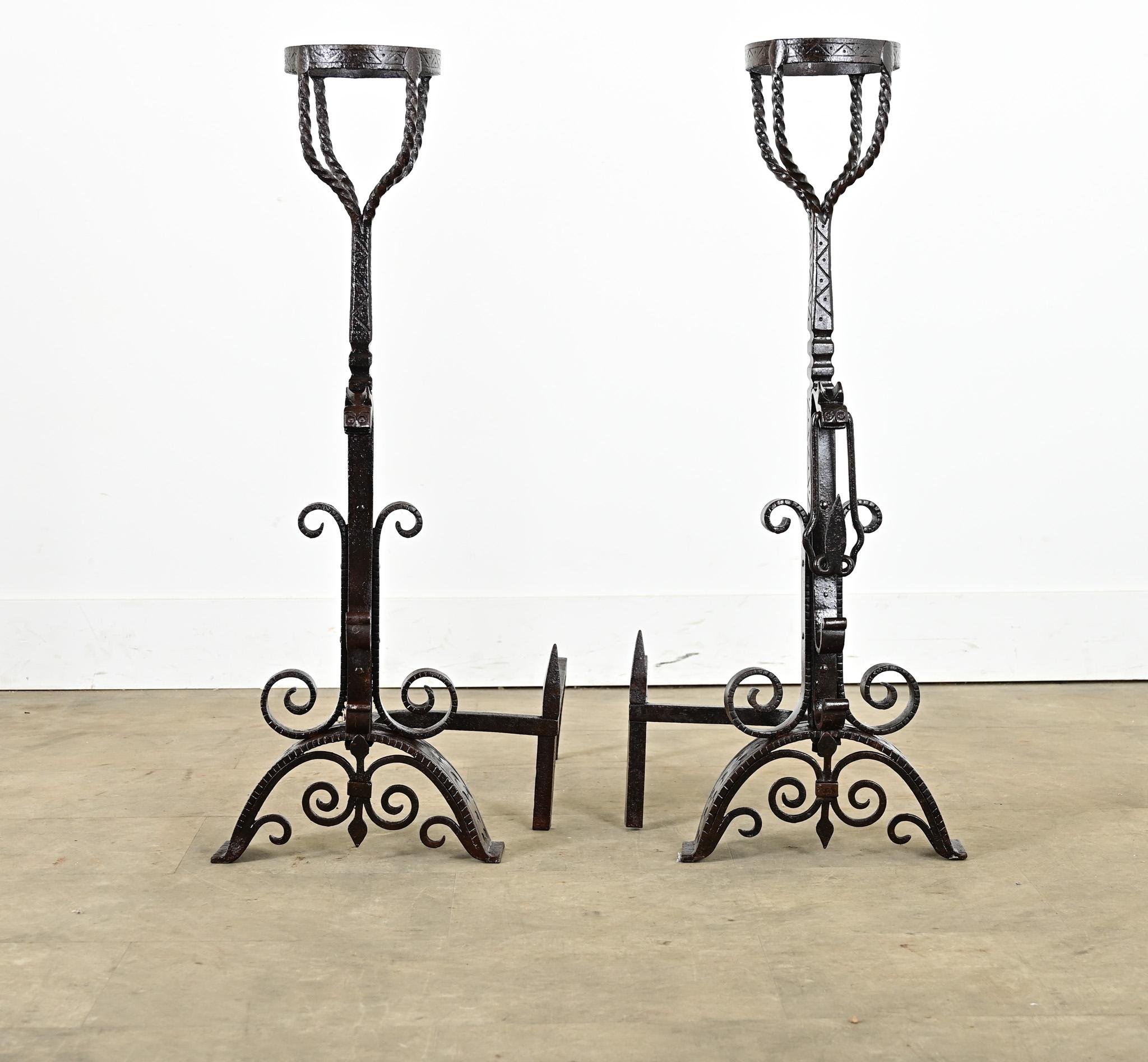 A towering pair of 18th century French forged, wrought iron andiron-chenets to watch over the hearth. They include a small basket at the top for warming, the rim impressed with a geometric pattern that is repeated on the column and contrasted by the