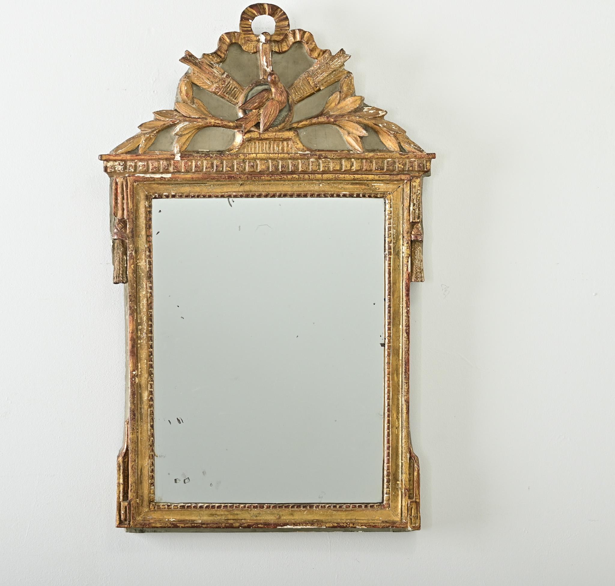 A spellbinding French trumeau style mirror, Louis XVI period (18th century). The painted and giltwood frame has an ornate pediment at the top with delicately carved imagery including a dove at center topped with a loop of ribbon draping around a