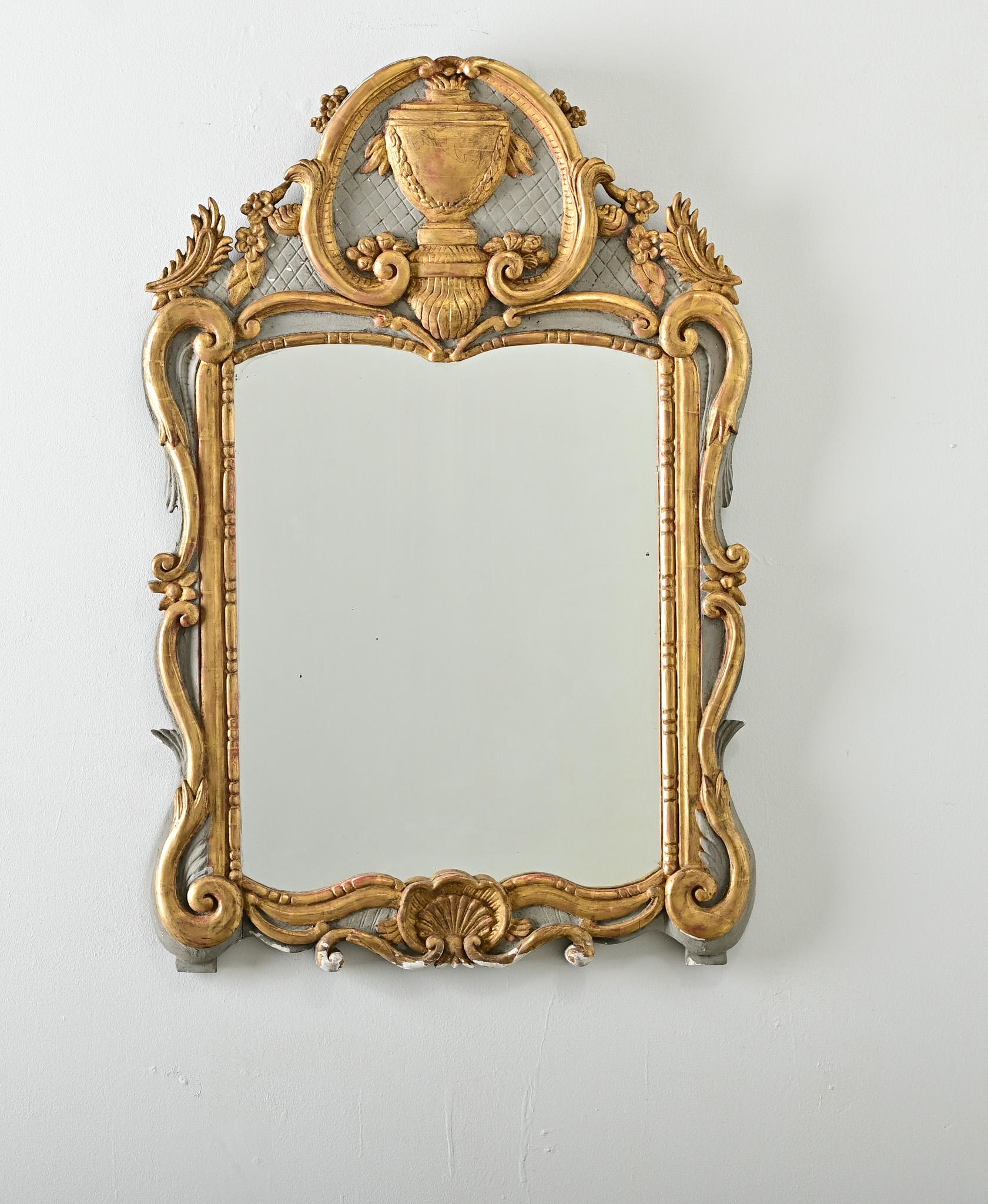 A magnificent 18th century French giltwood trumeau mirror in the style of Louis XVI, the thick rococo carvings around the (French gray) painted frame appear even more theatrical under a layer of gold. At the top of the piece is a near spherical