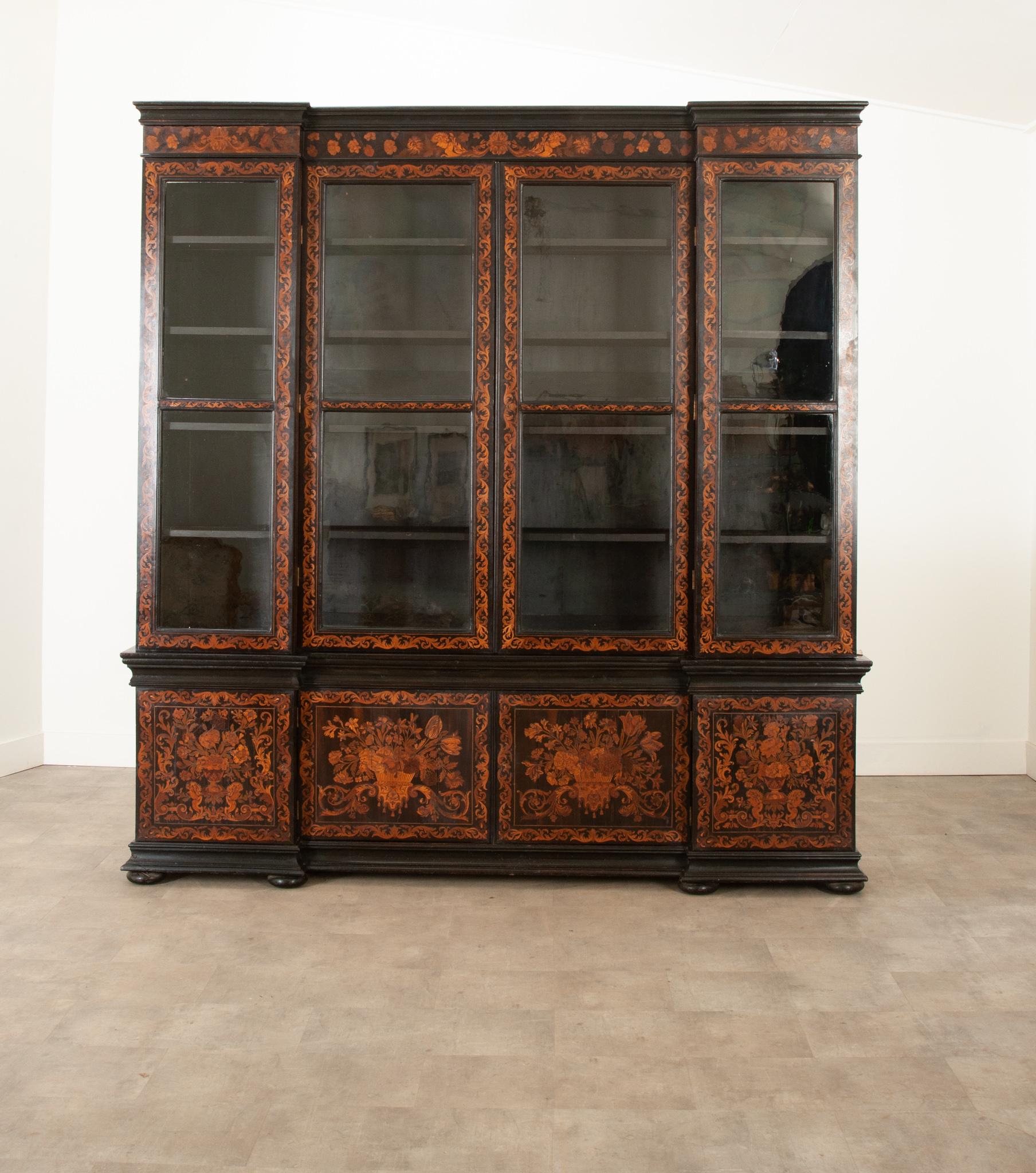 A breathtaking hand carved ebony cabinet with over the top marquetry designs! Built in the 1790’s this rare and fine breakfront bookcase is in outstanding antique condition. All the doors display hand rolled glass panes sounded in detailed inlay.