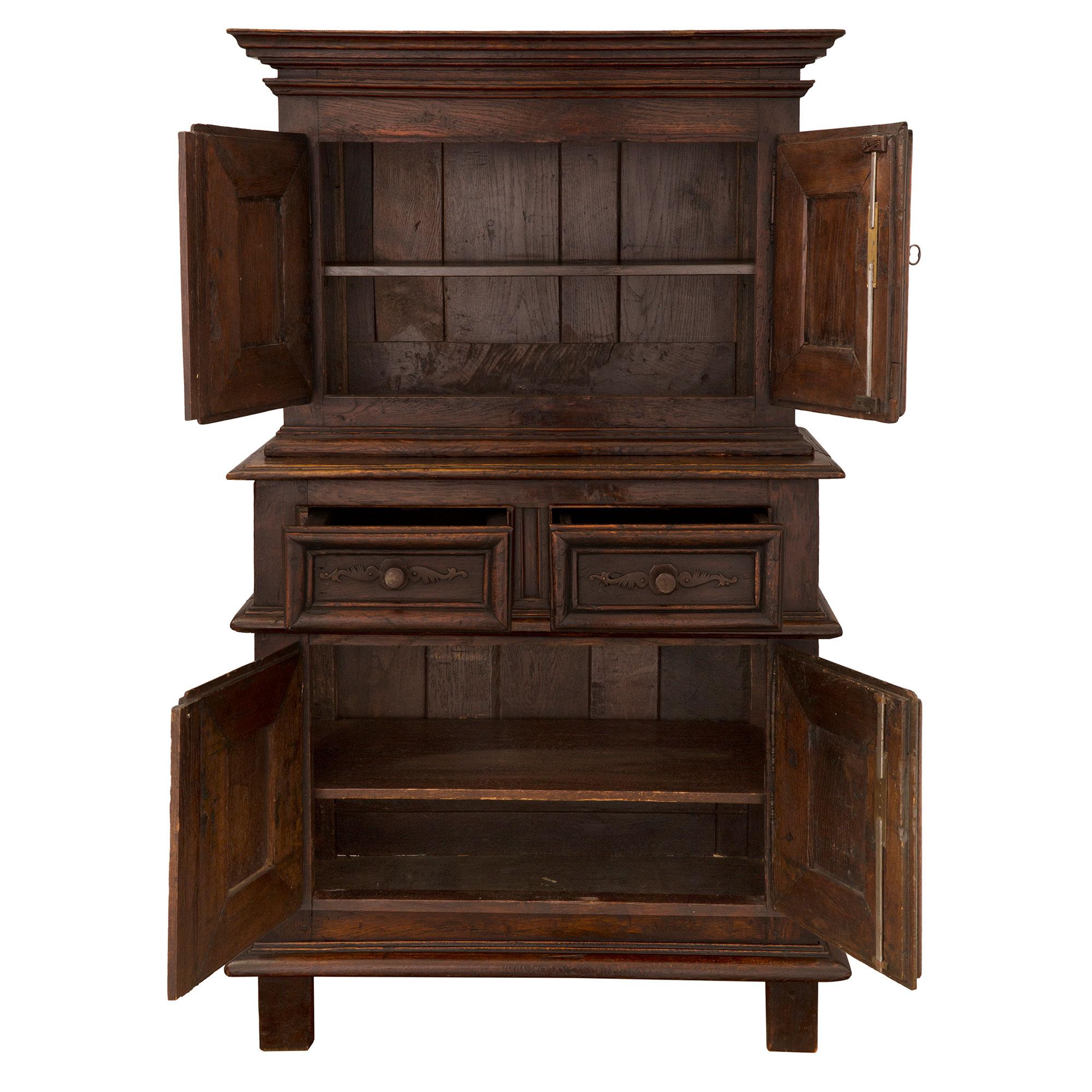 Belle armoire à deux corps en chêne de style Louis XIII du XVIIIe siècle. Le meuble à quatre portes et deux tiroirs est surélevé par quatre supports rectangulaires sous le tablier droit moucheté. Les quatre portes présentent des motifs en creux