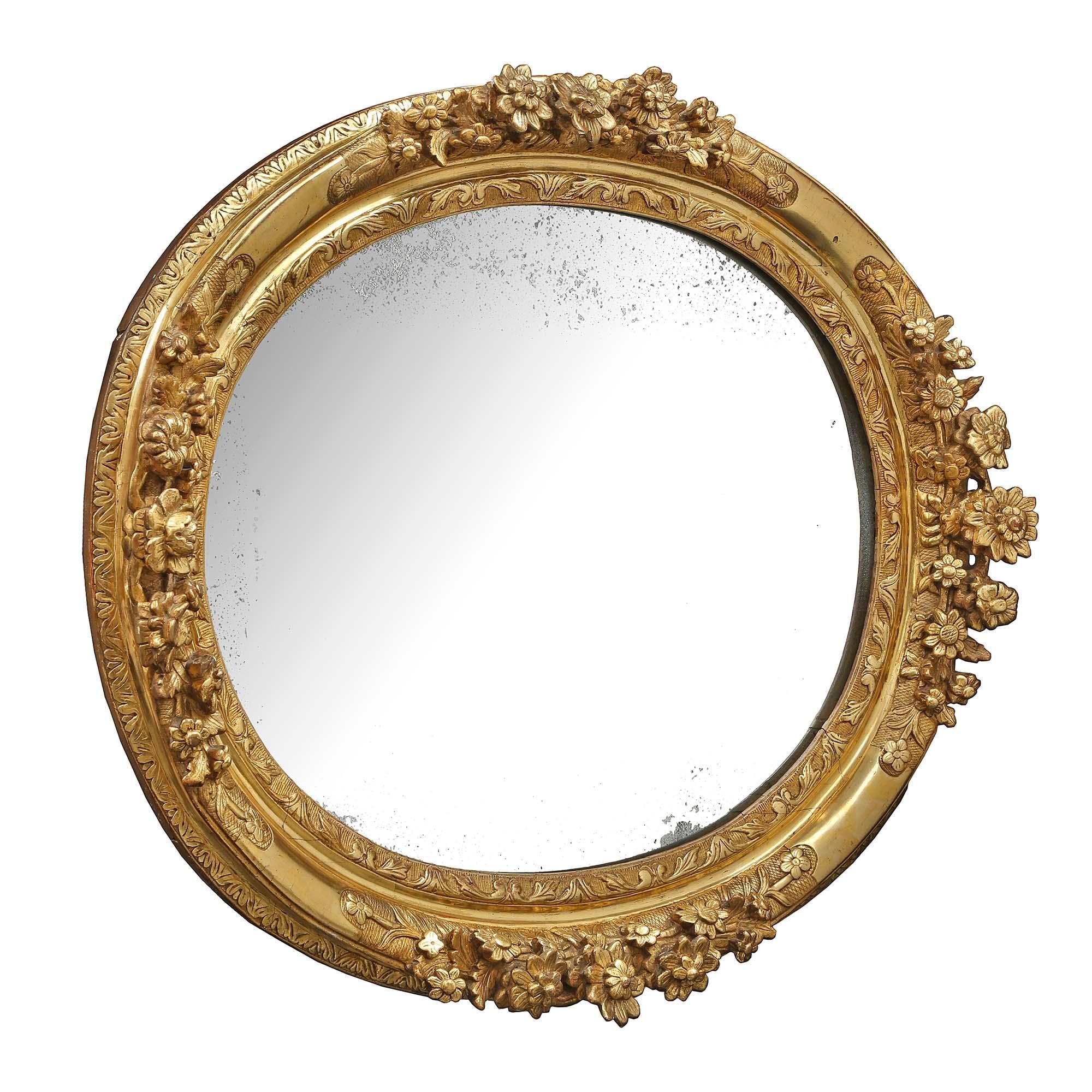 A stunning French early 18th century Louis XIV Period finely carved giltwood mirror. This oval mirror has an interior scrolled designed border and large protruding carved foliate frame with acanthus leaf designed trim. With all original mirror plate
