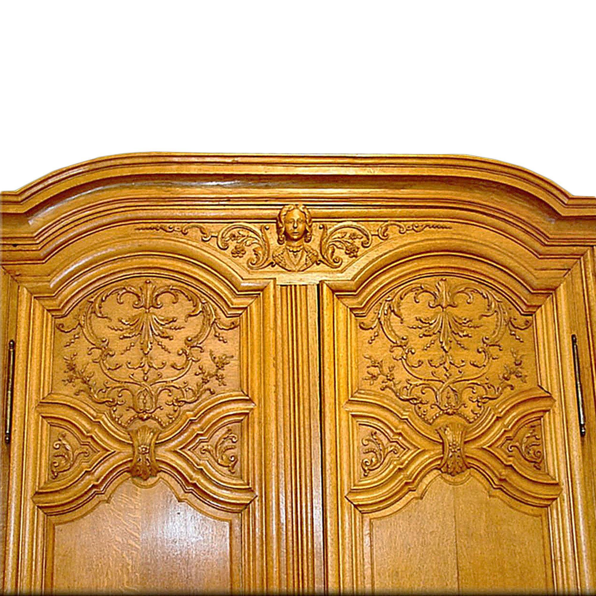 An exceptional French 18th century Louis XIV period two-door Oak armoire with extremely fine carvings of flowers, garlands, and at the top, carvings of a face. All original hardware.