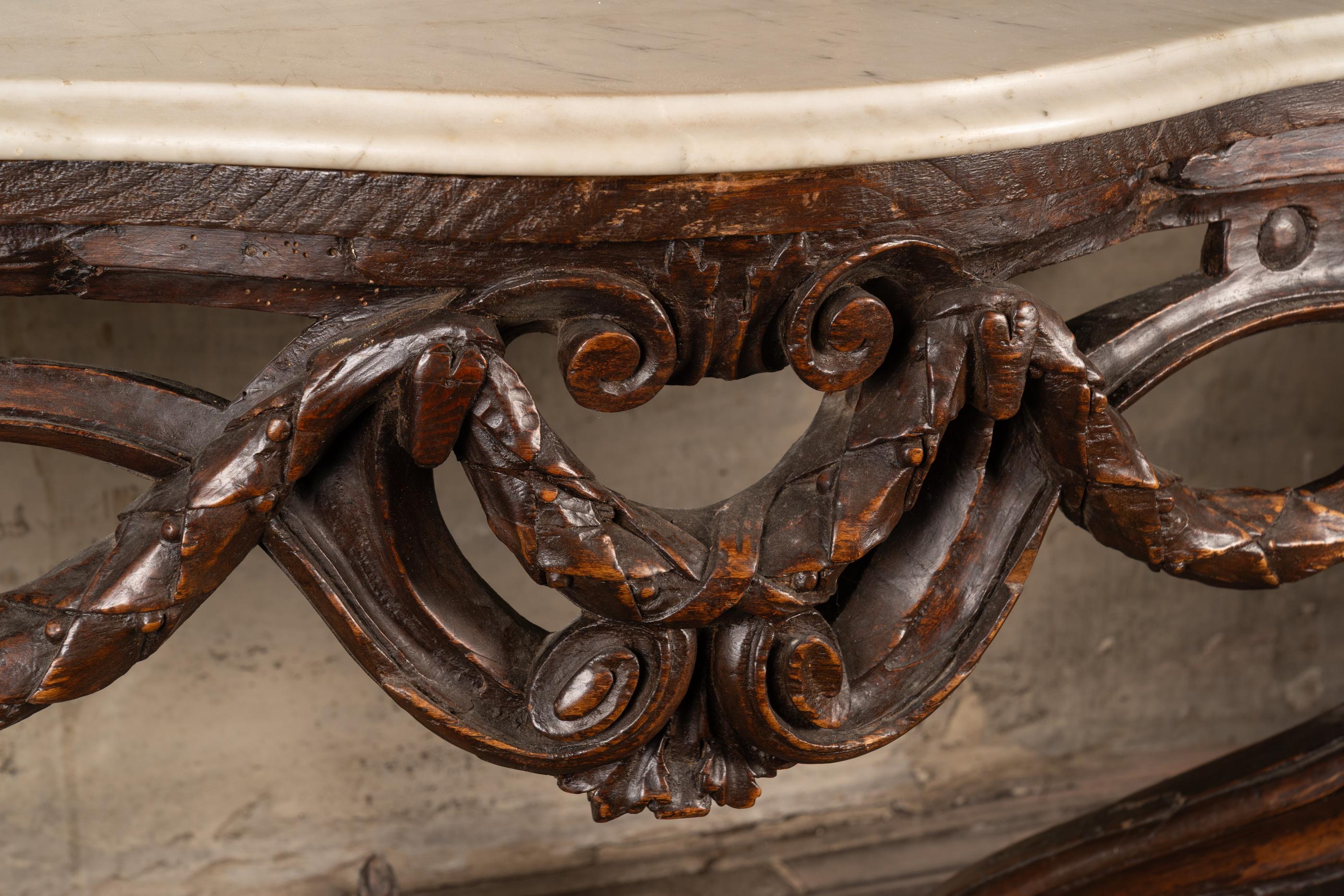 Beautiful French Louis XV console made of walnut dating back to the 18th century. The piece features a contoured white marble top. Below rests detailed carvings; note the roses flanked by a greek key design at the base, the pair of roses at the top