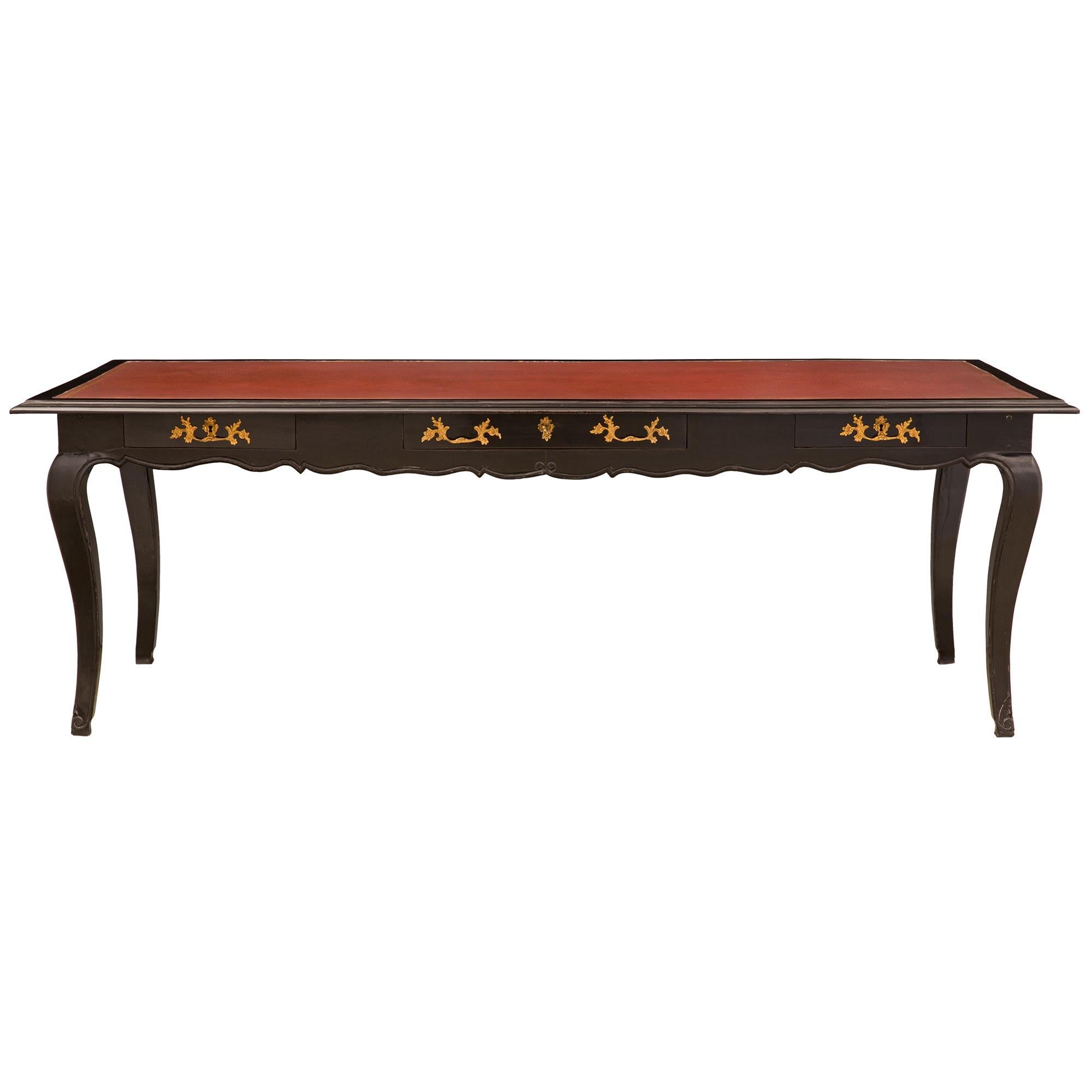 A striking and large-scale French 18th century Louis XV period ebonized fruitwood and ormolu library table/desk. The desk is raised by elegant cabriole legs with fine foliate feet and a lovely carved filet; which leads up each leg and extends along